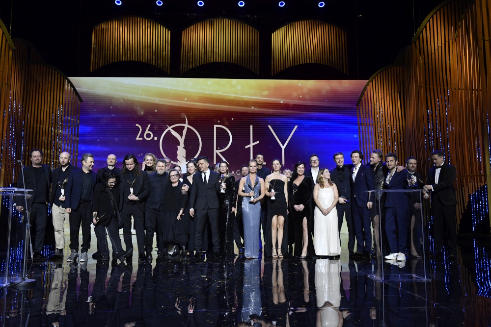 Duża grupa osób w strojach wieczorowych na scenie, o tle napis "ORŁY"