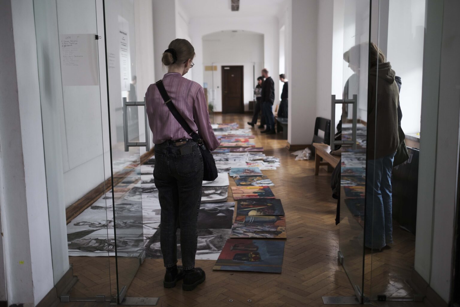 osoba w korytarzu, przed nią prace ułożone na podłodze