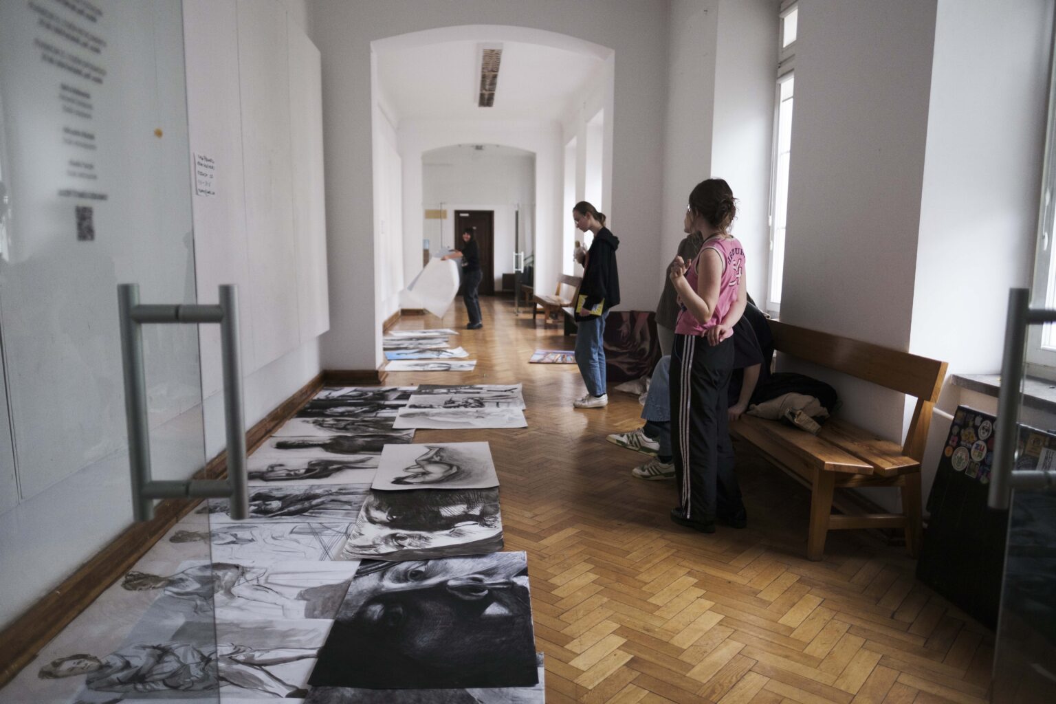 osoby w korytarzu, prace ułożone na podłodze