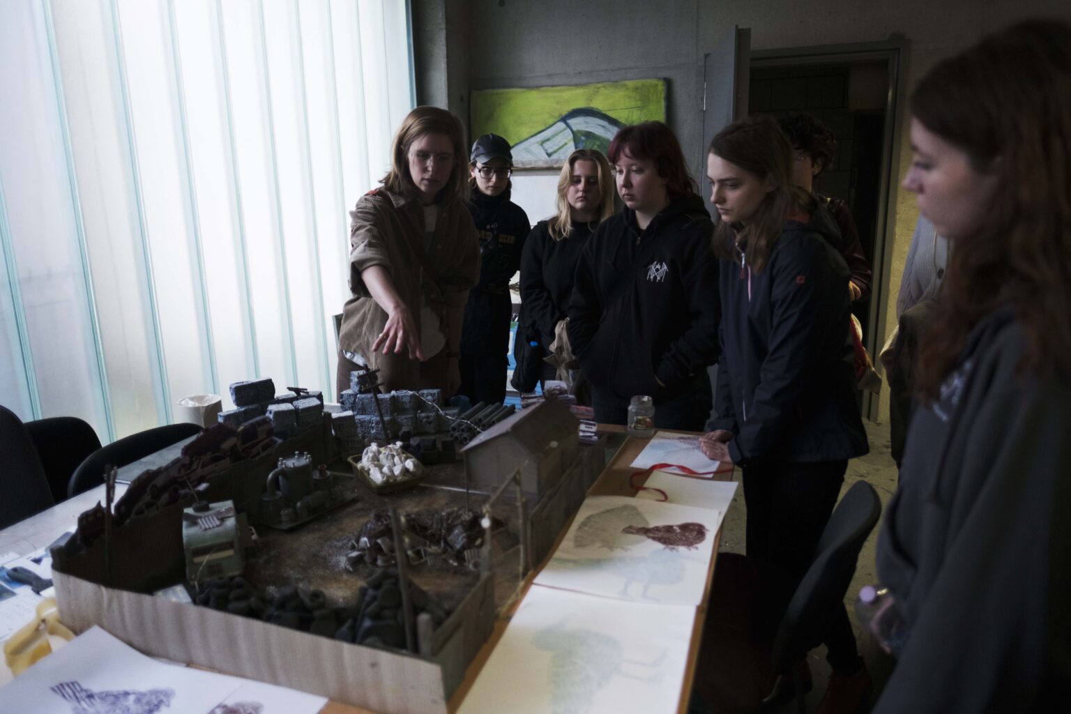 osoby w pracowni, młoda kobieta tłumaczy coś wskazując ręką na makietę