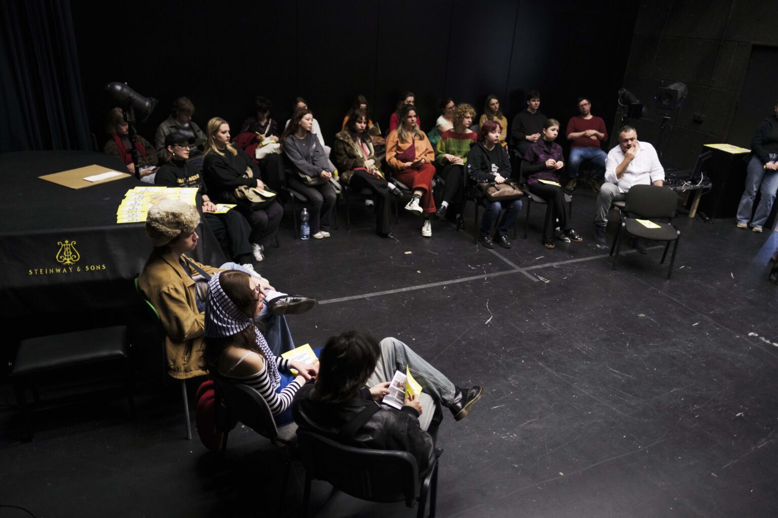 grupa osób siedzi na krzesłach, na scenie