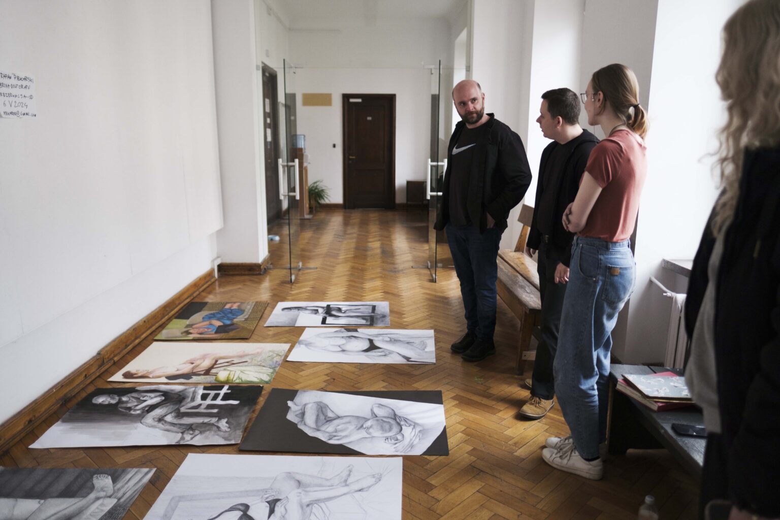 trzy osoby w korytarzu, przed nimi prace ułożone na podłodze