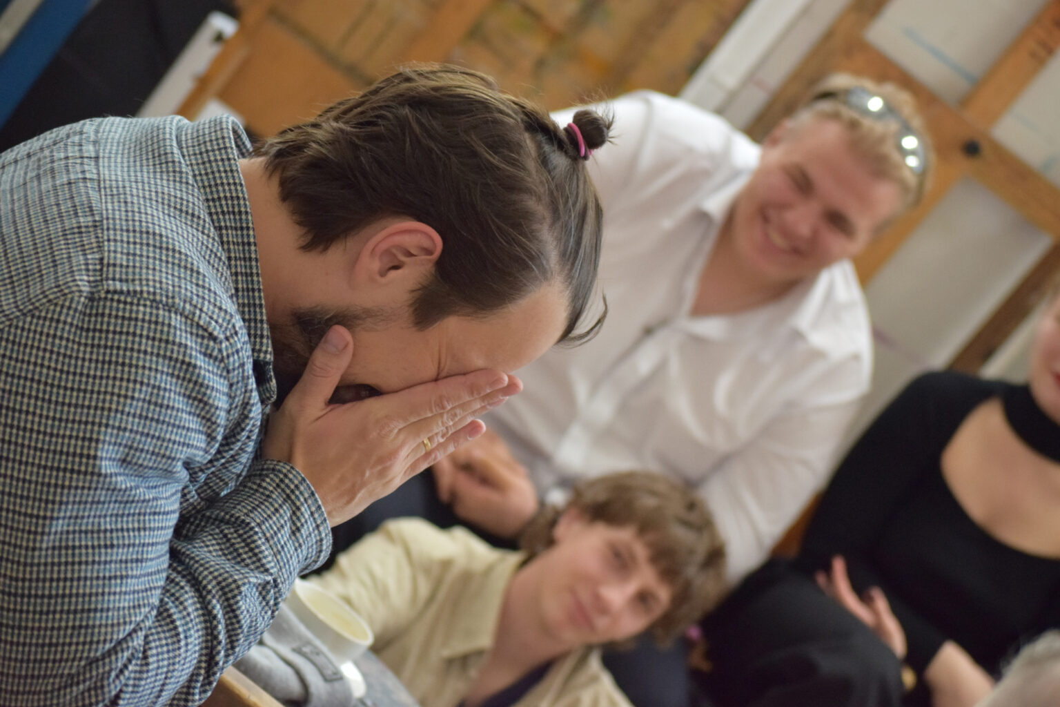 Mężczyzny z włosami związanymi w małą kitkę na czubku głowy chowa twarz w dłoniach