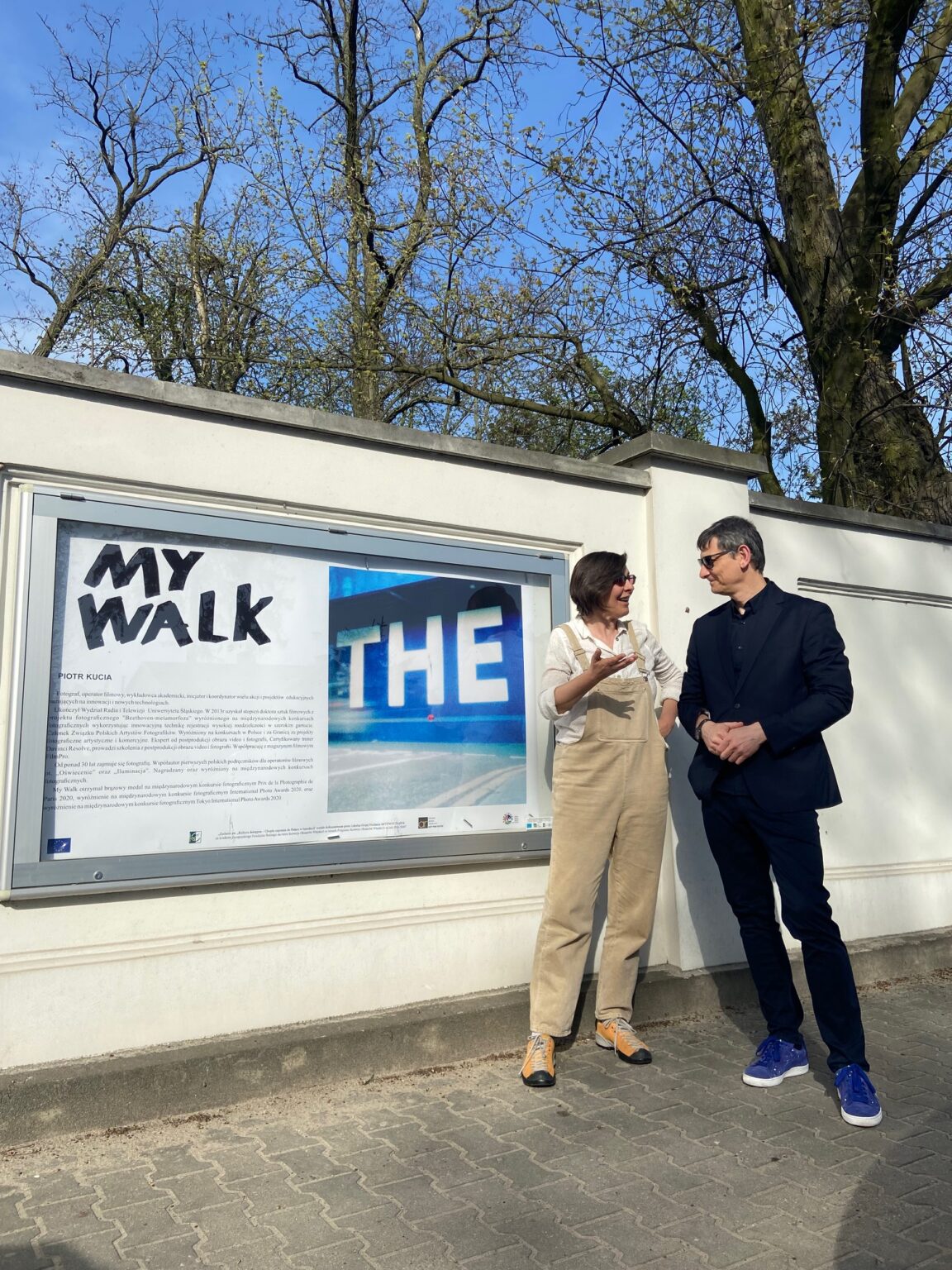 Dwie osoby stoją przy gablocie, której prezentowane są zdjęcia