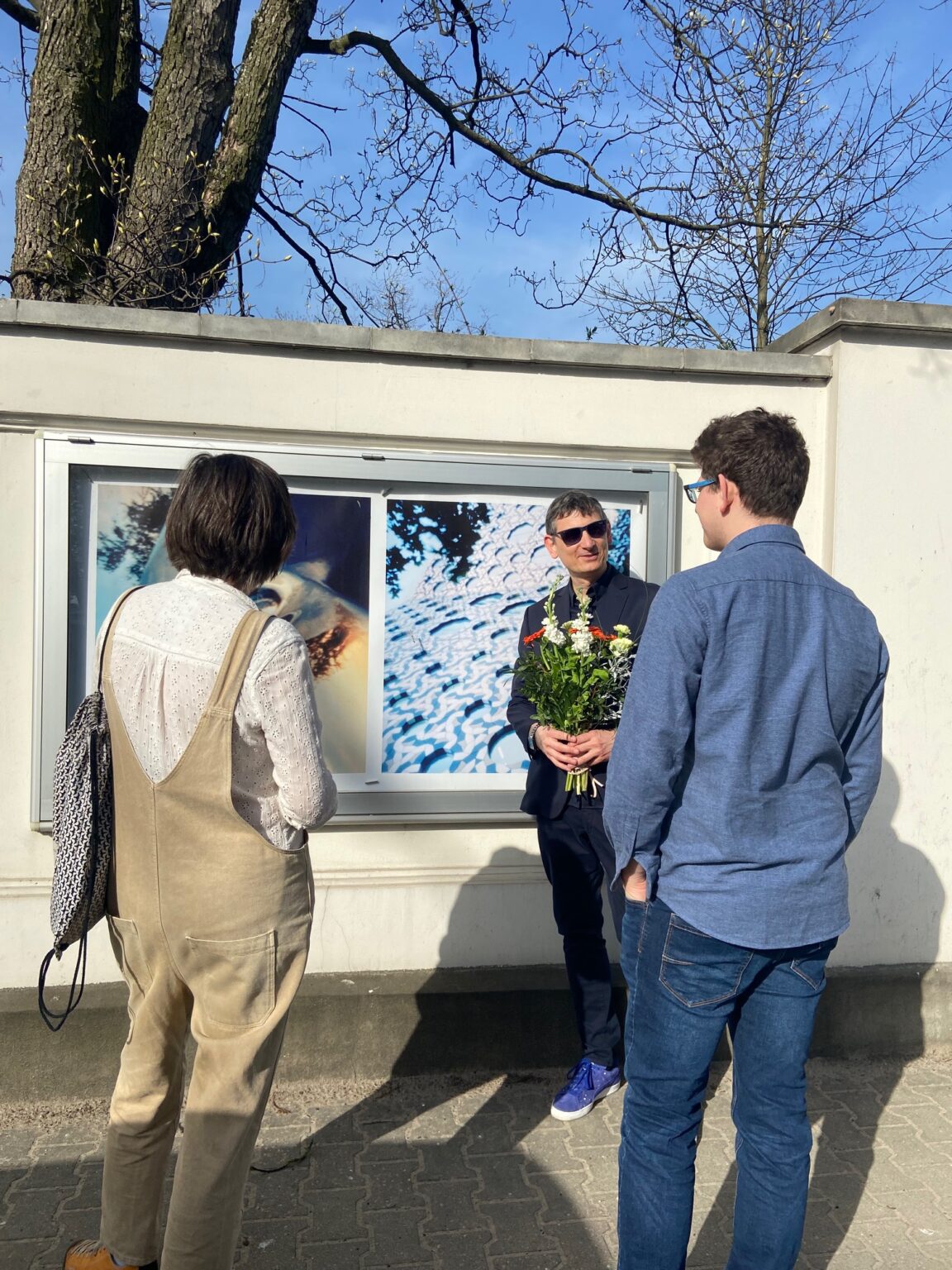 Trzy osoby stoją przy gablocie, której prezentowane są zdjęci