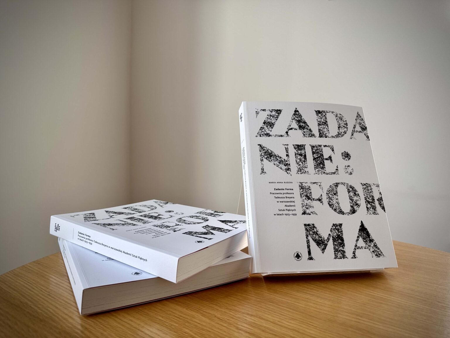 Wyeksponowana książka na blacie stołu. Obok (po lewej stronie) 2 egzemplarze jeden na drugim