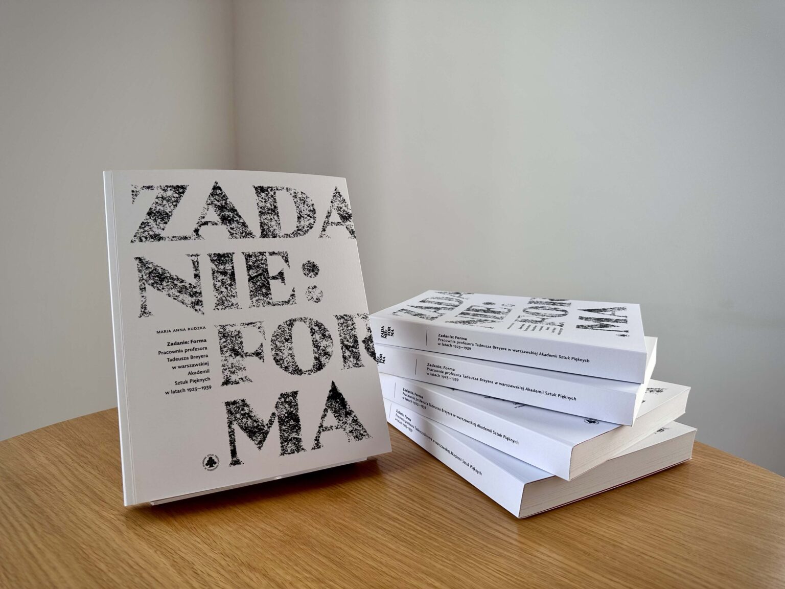 Otwarta książka na blacie stołu. Obok (po prawej stronie) 4 egzemplarze jeden na drugim