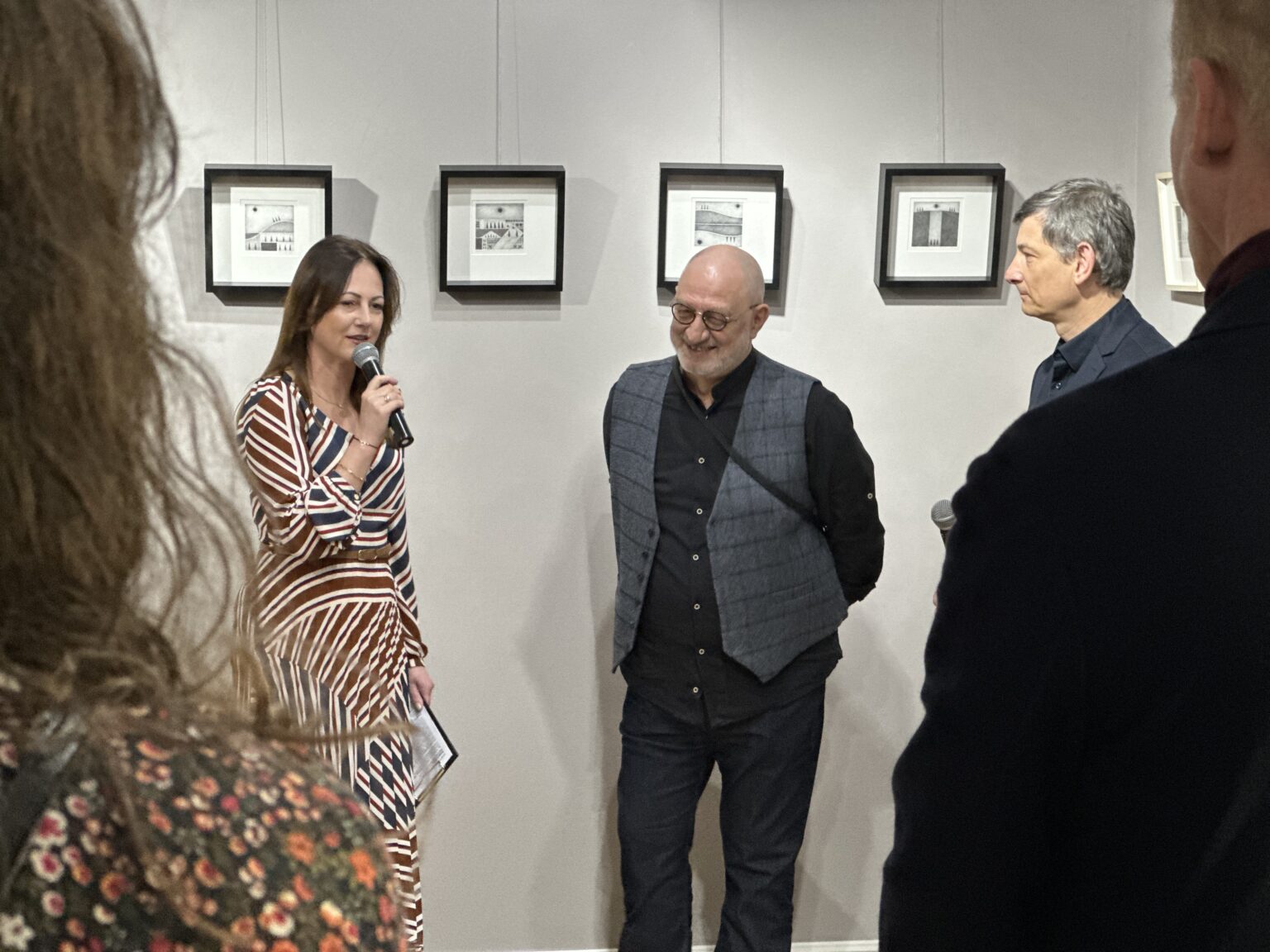 Trzy osoby na tle kwadratowych obrazów w czarnych ramkach