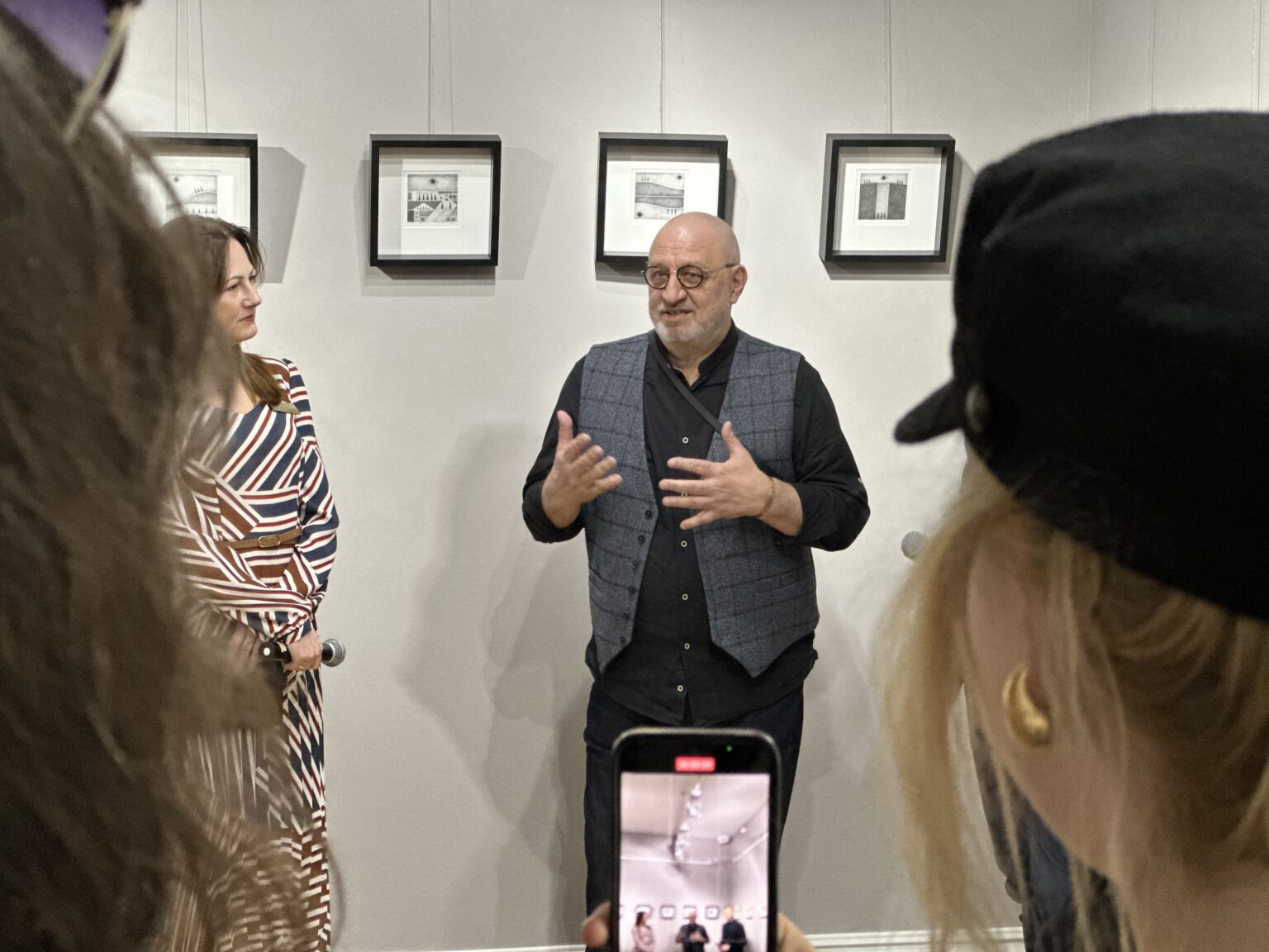 Trzy osoby na tle kwadratowych obrazów w czarnych ramkach