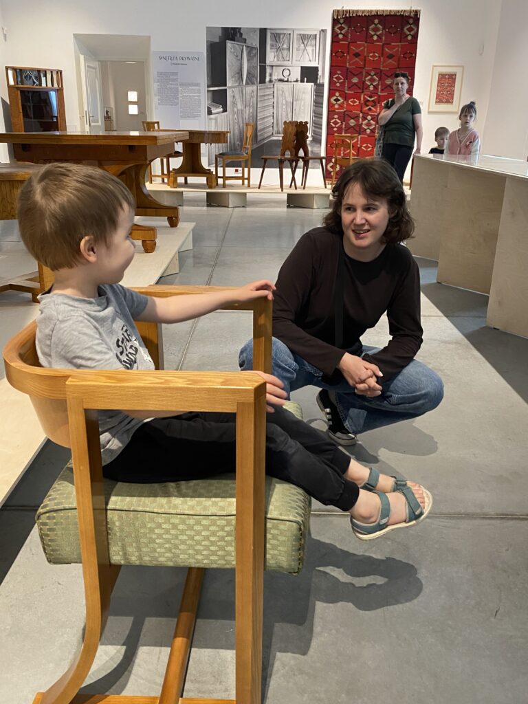 Chłopiec siedzi w fotelu, obok prowadząca oprowadzanie