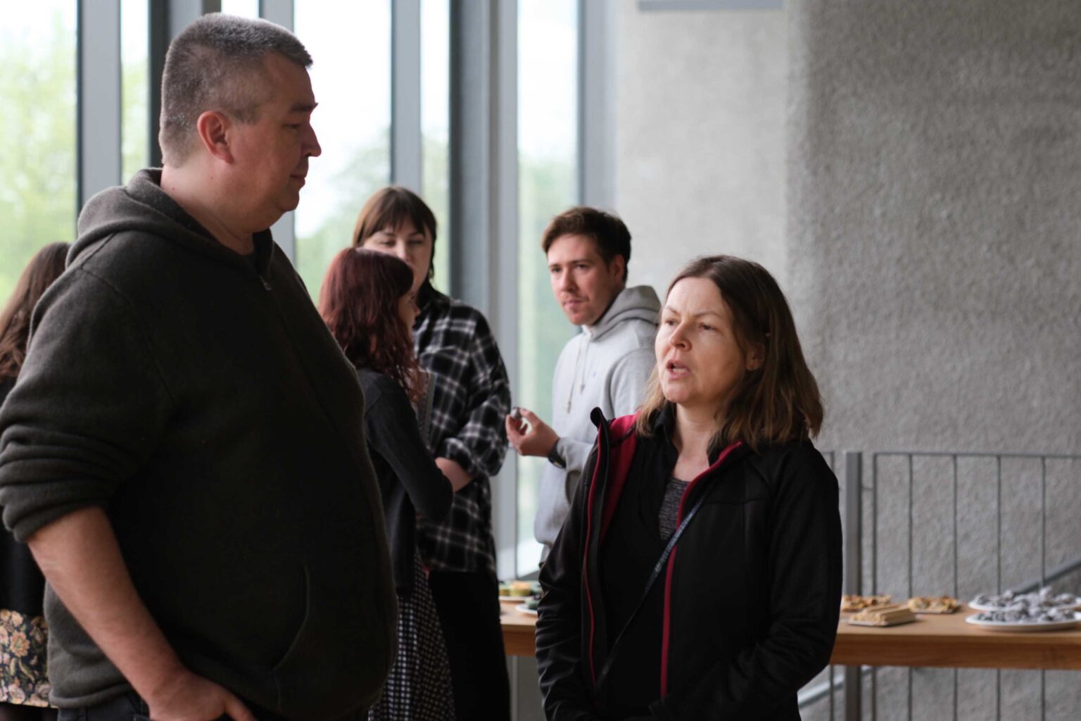 dwie osoby rozmawiają, kilka osób w tle