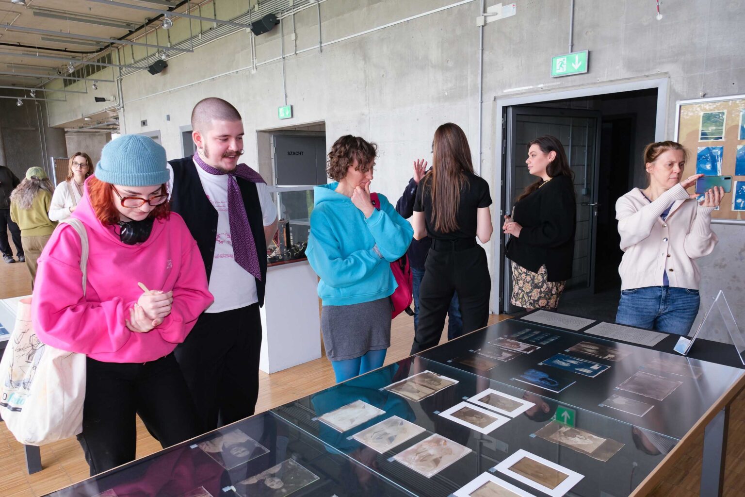 grupa osób przed gablotą ze zdjęciami