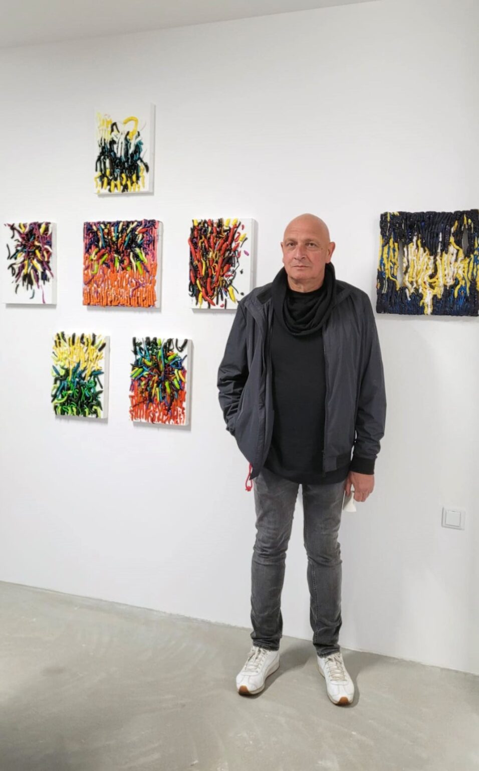 Mężczyzna stoi na tle ściany, na której prezentowane są obrazy