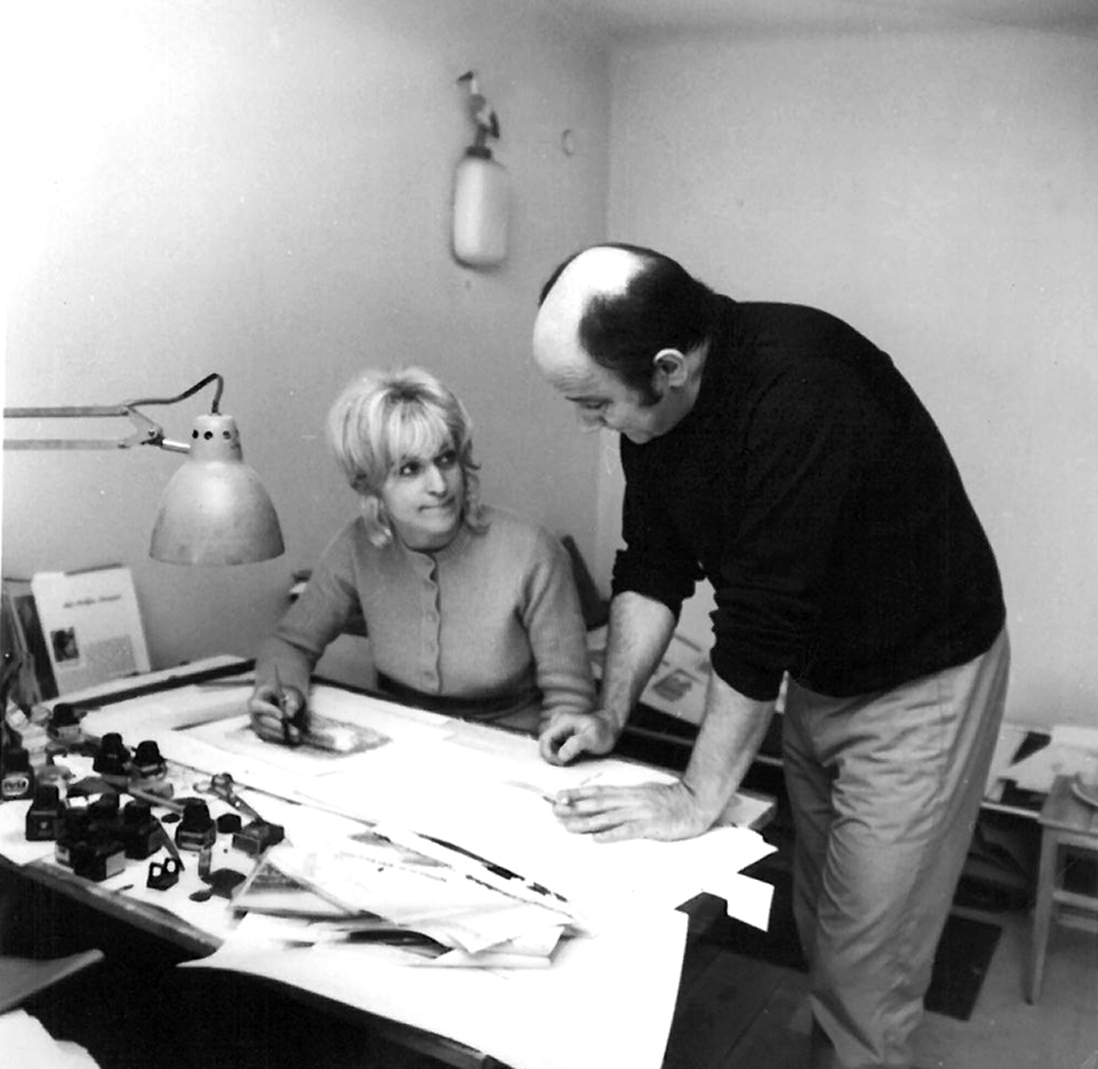 Kobieta siedzi przy biurku. Mężczyzna obok wsparty o blat biurka. Czarno-białe zdjęcie