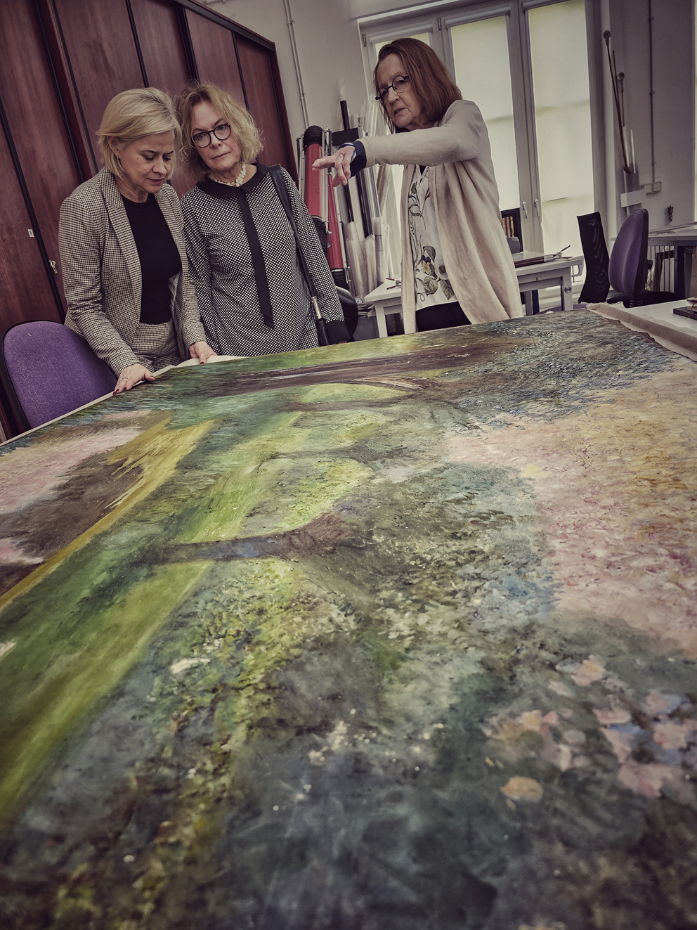 Trzy osoby w pracowni przy stole z obrazem
