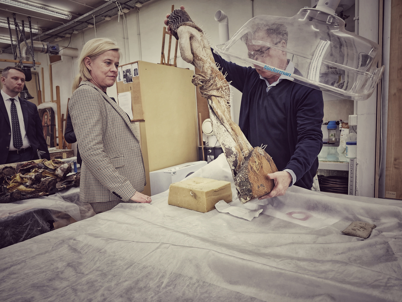 Dwie osobyw pracowni. Mężczyzna prezentuje drewnianą figurę Chrystusa