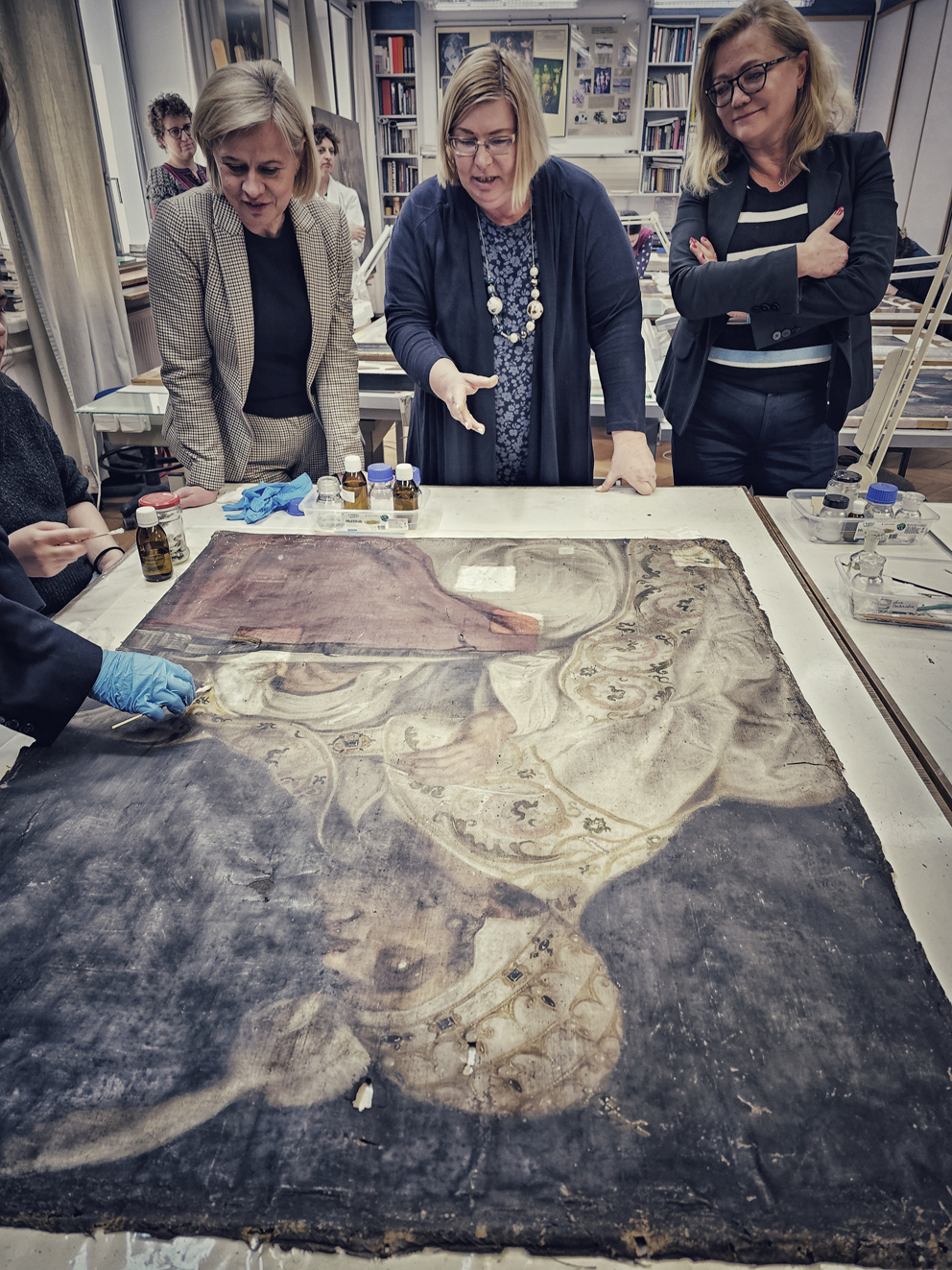 Trzy osoby w pracowni przy stole z obrazem