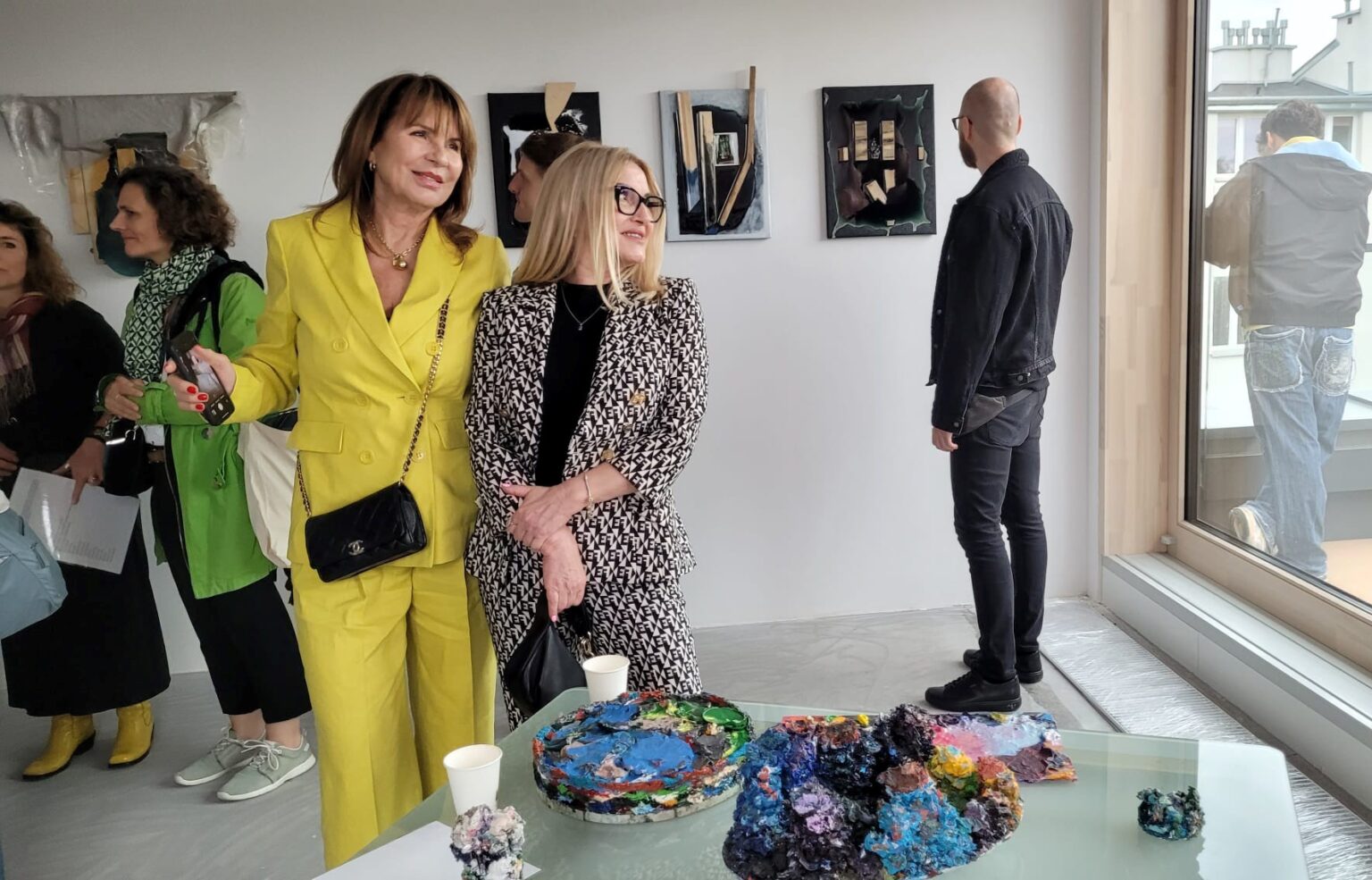 Przestrzeń wystawy. Obrazy w tle. Na pierwszym planie dwie uśmiechnięte kobiety