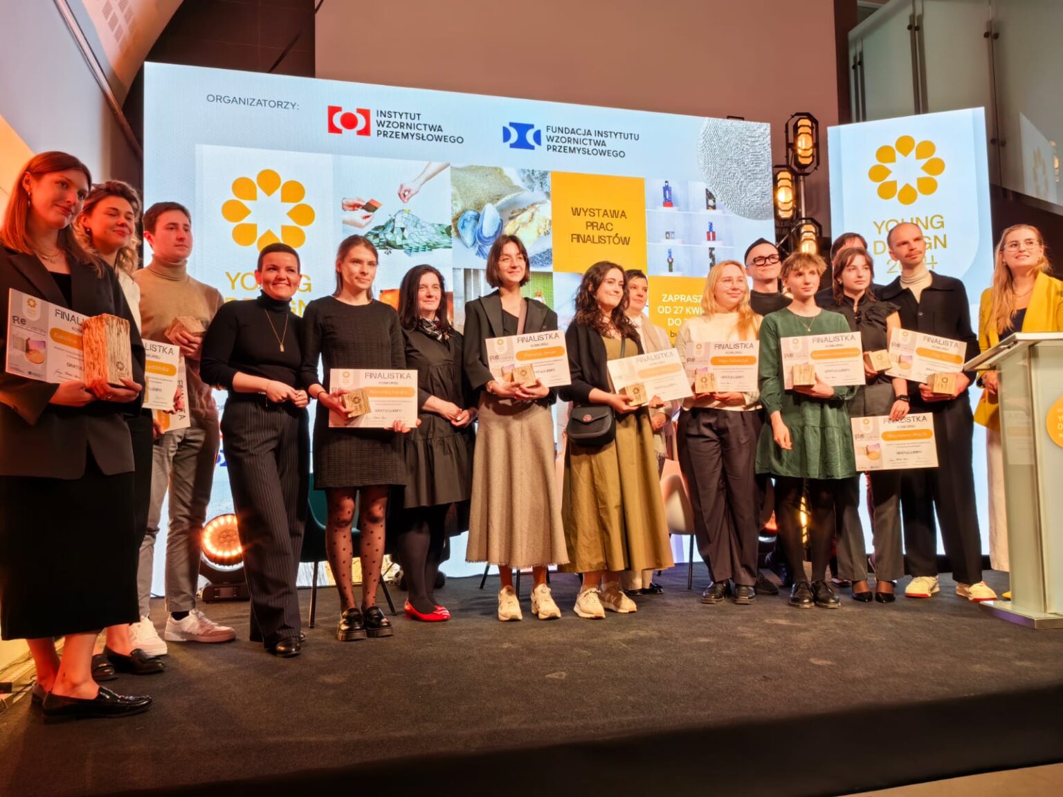 Grupa osób na scenie. Trzymają dyplomy