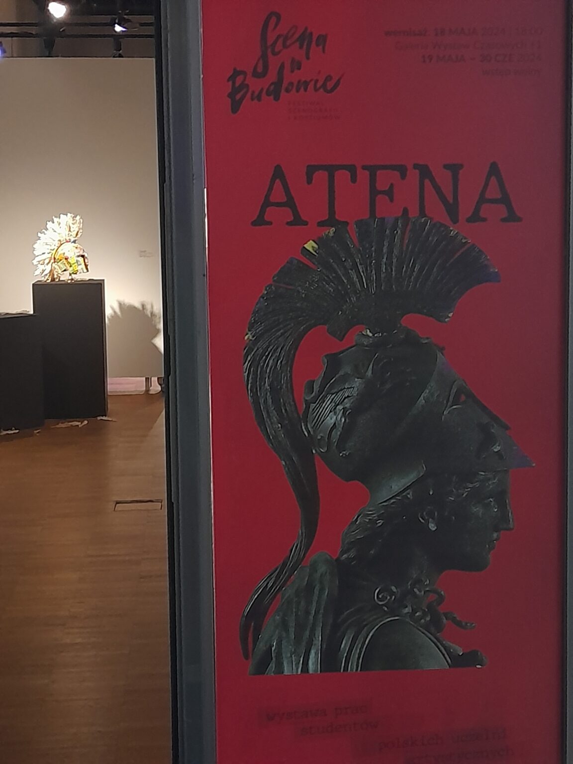 Na pierwszym tle grafika z napisem Atena i elementem graficznym na czerwonym tle. Na drugim planie: obiekt prezentowany na wystawie.