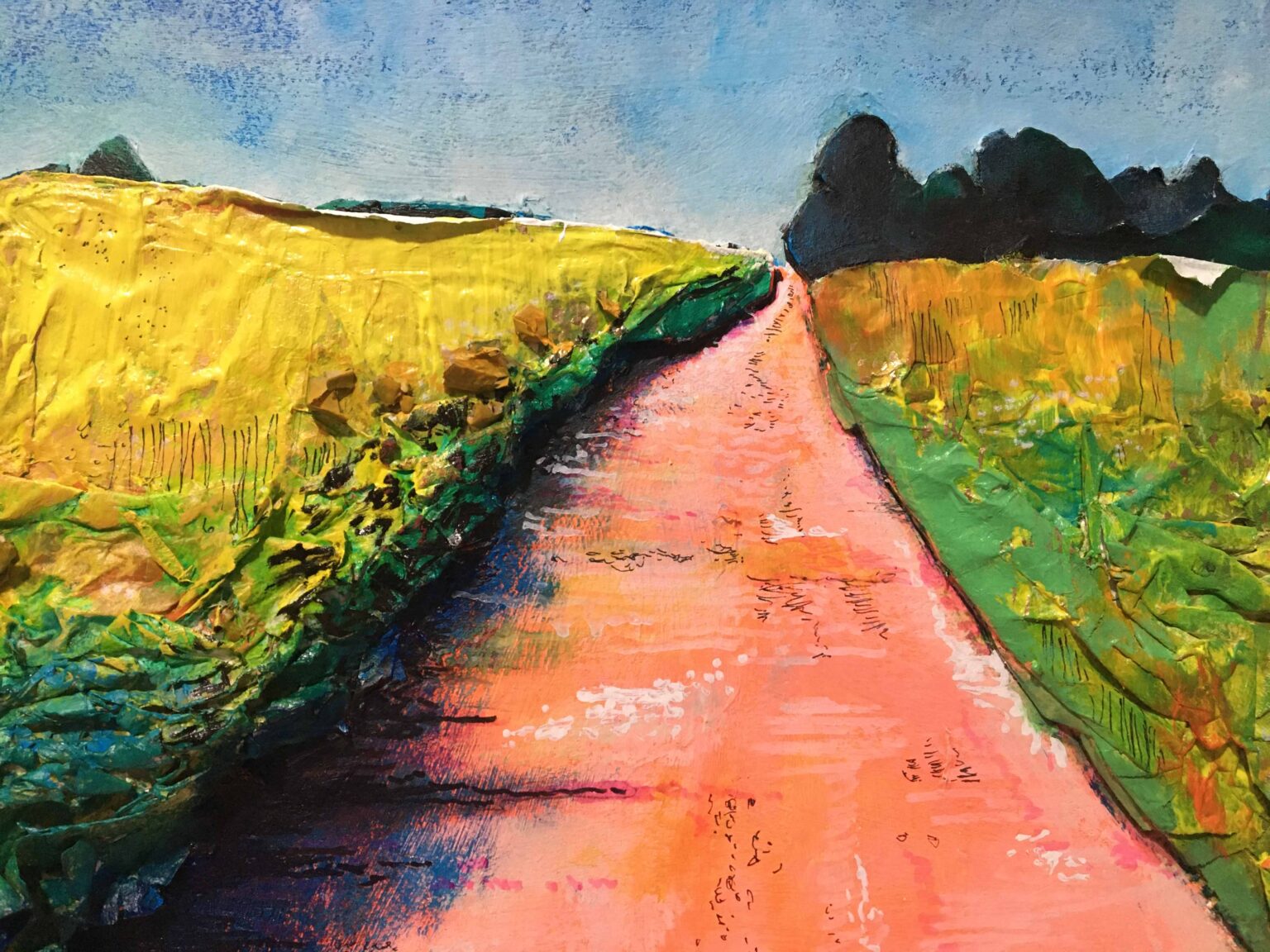 Droga ceglana, po lewej stronie łąka z żółtymi kwiatami, błękitne niebo