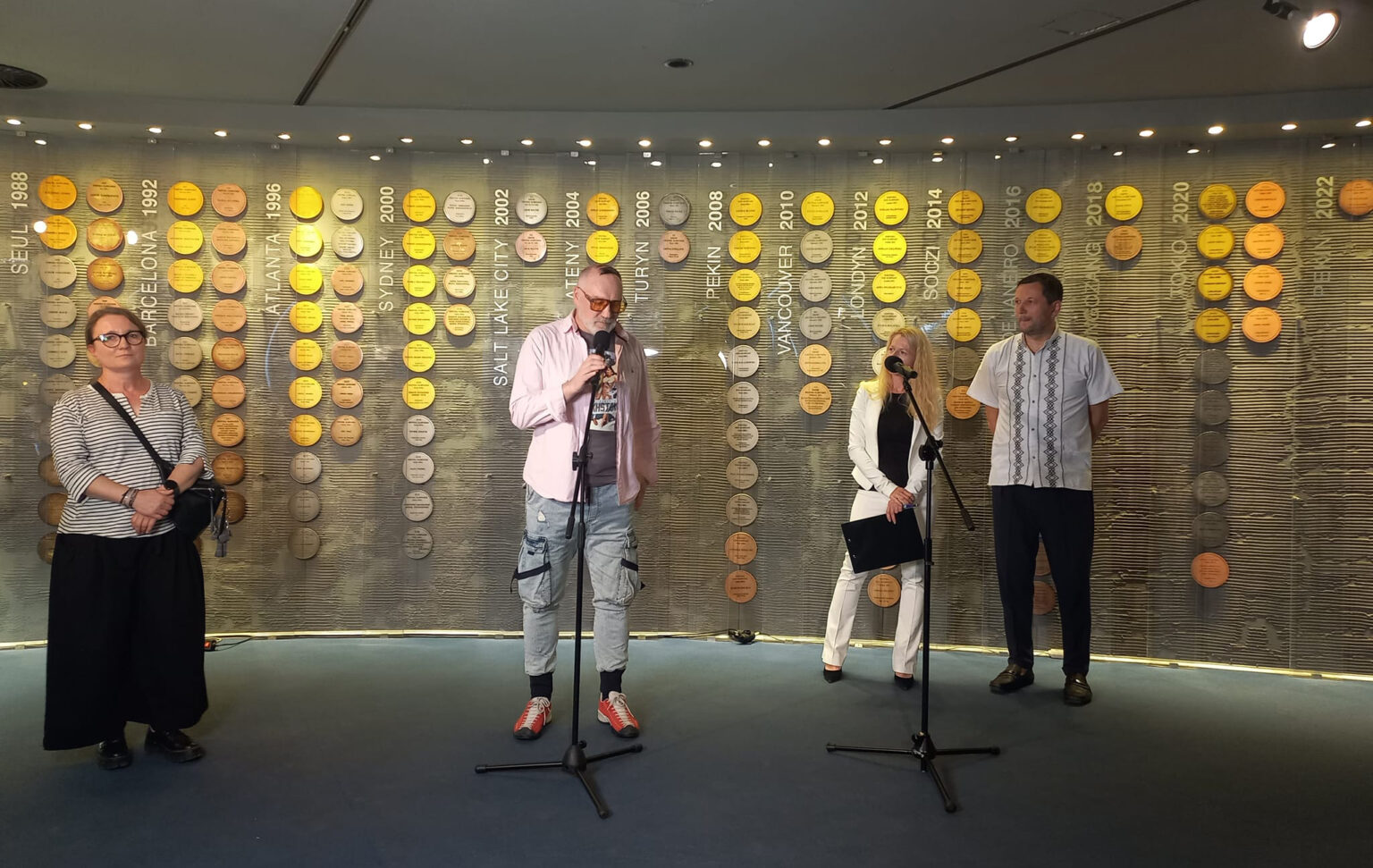 Cztery osoby. Mężczyzna przy mikrofonie. W tle okrągłe żółte elementy na ścianie.