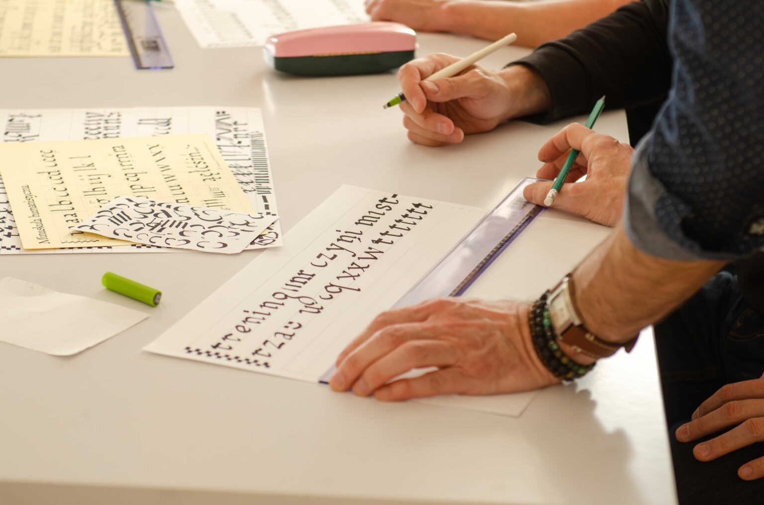 zbliżenie na dłonie z linijką, powyżej kartka papieru z wykaligrafowanymi literami