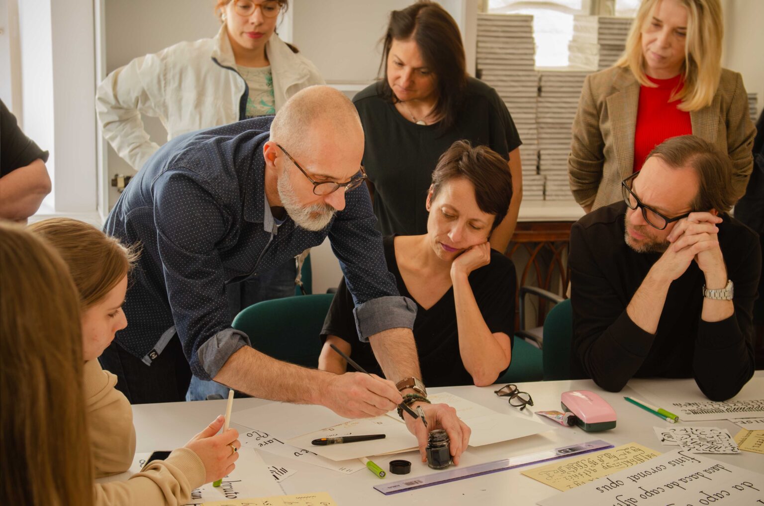 grupa osób przy stole w pracowni, mężczyzna kaligrafuje