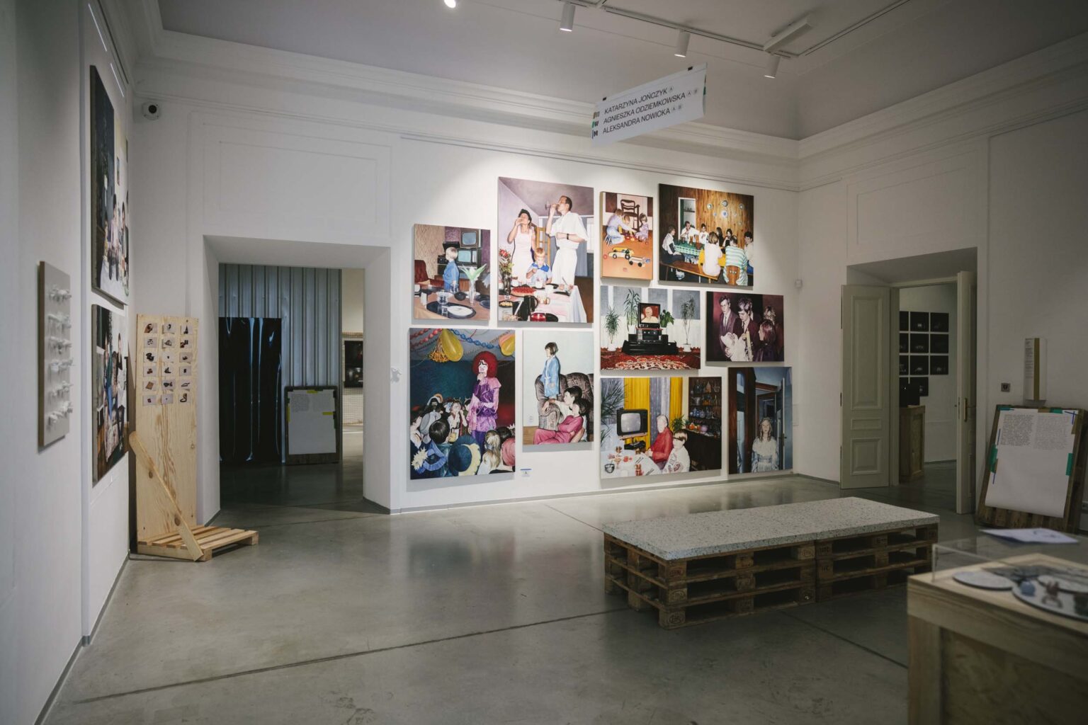 Widok ściany z oddali, na której prezentowane są kolorowe obrazy z dużych formatach