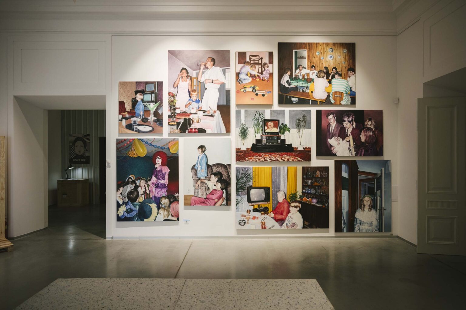 Widok ściany z oddali, na której prezentowane są kolorowe obrazy z dużych formatach