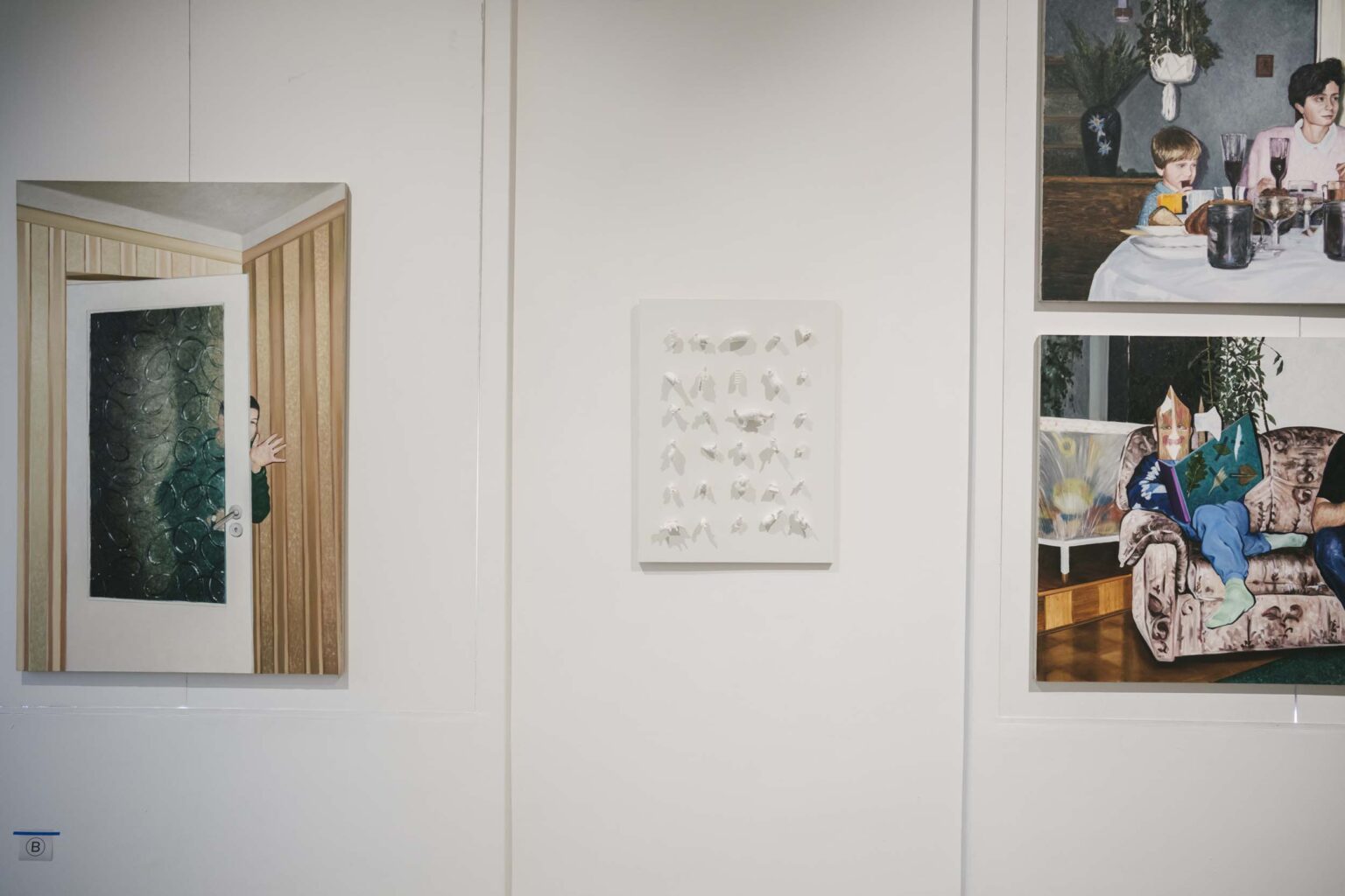 Biała tablica z wypukłymi figurkami zwierząt w białym kolorze, po bokach fragmenty obrazów