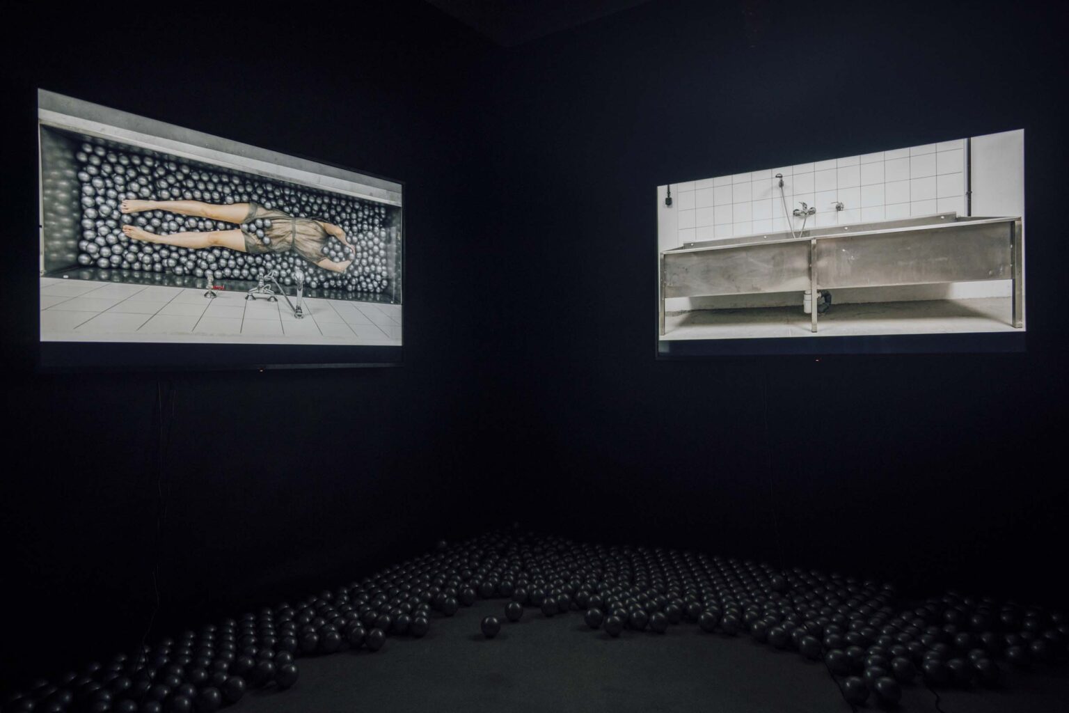 Dwa ekrany prezentujące widoo w ciemnej sali; srebrne kulki wielkości piłeczek tenisowych na podłodze