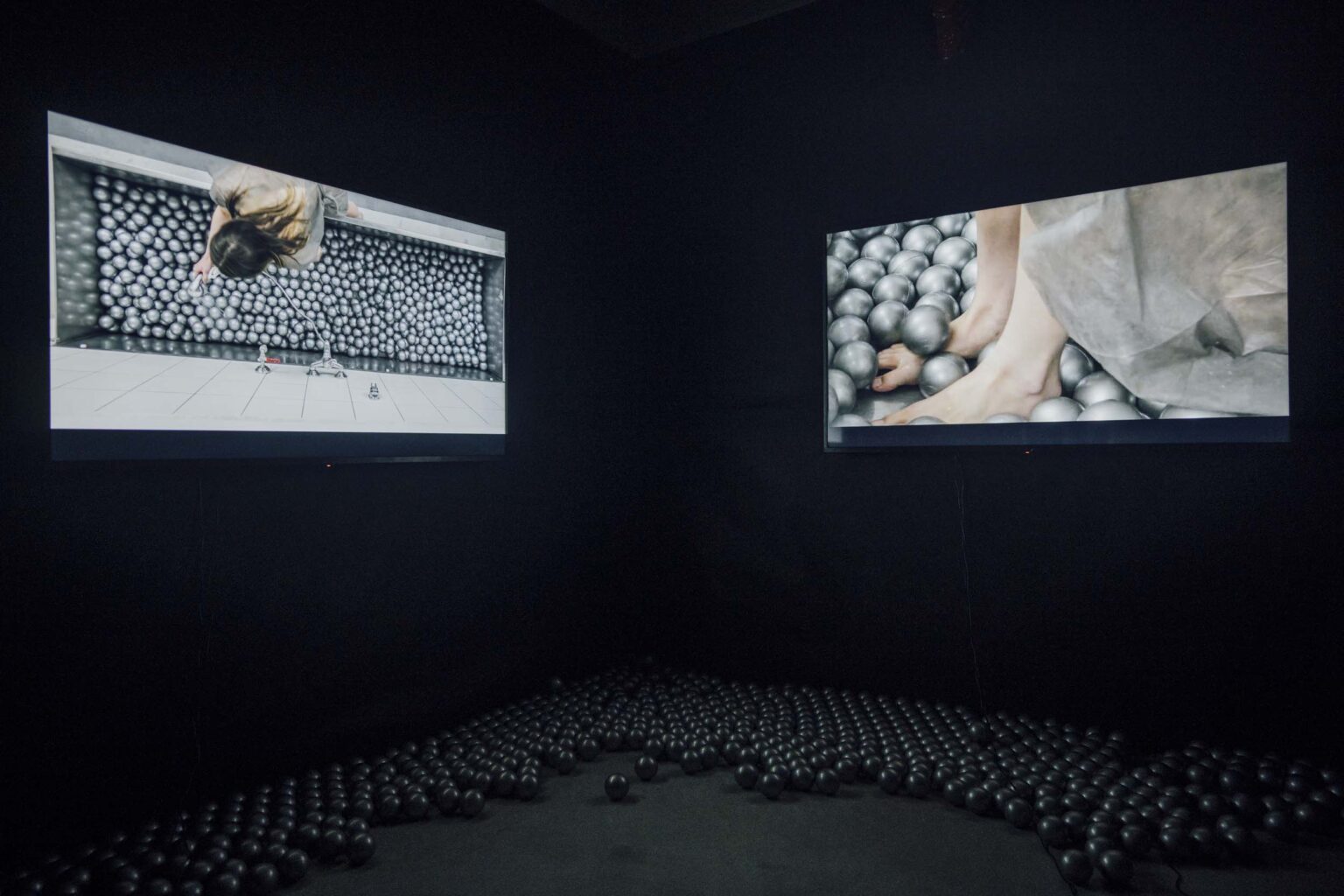 Dwa ekrany prezentujące widoo w ciemnej sali; srebrne kulki wielkości piłeczek tenisowych na podłodze
