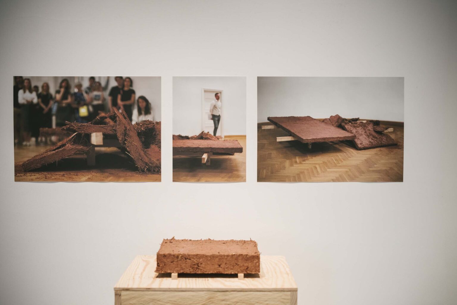 zdjęcia na ścianie, kadzielnica we wnęce ściany i obiekt gliniany na drewnianym postumencie