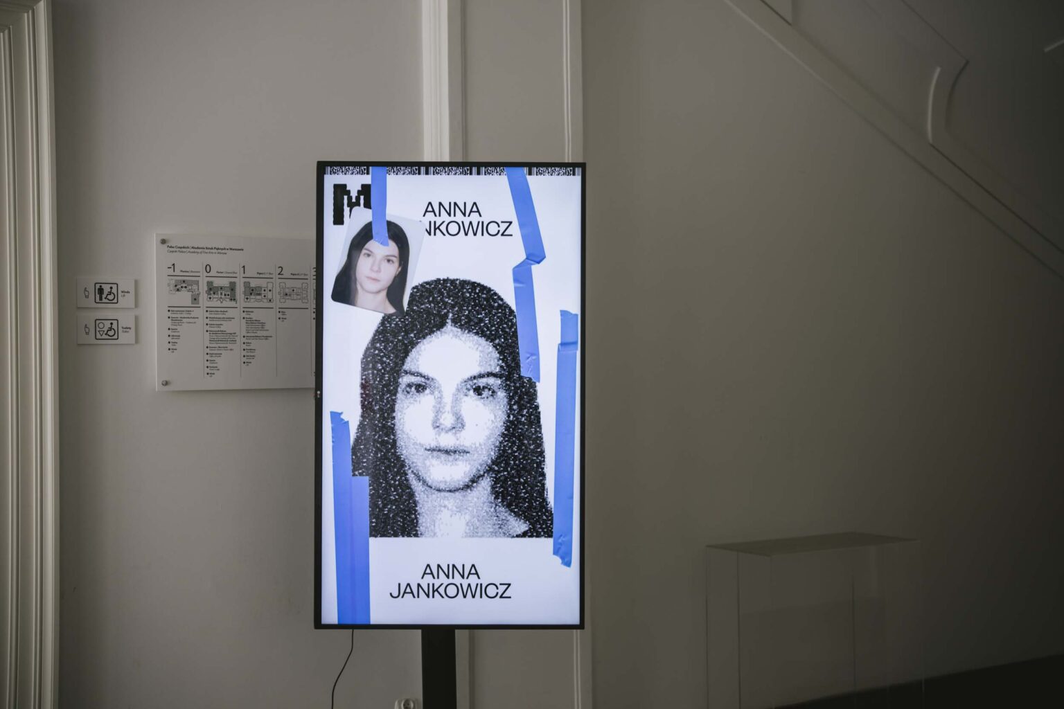 Pionowy ekran przedstawia czarn-białe zdjęcie dziewczyny, elementy identyfikacji wizualnej wystawy