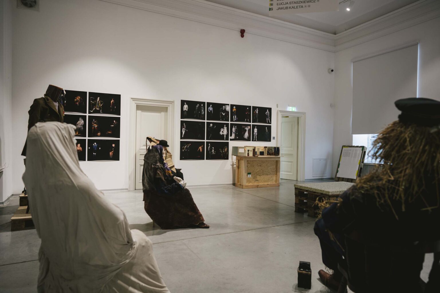 Sylwetki naturalnych rozmiarów siedzą w przestrzeni wystawy, rysunki w tle