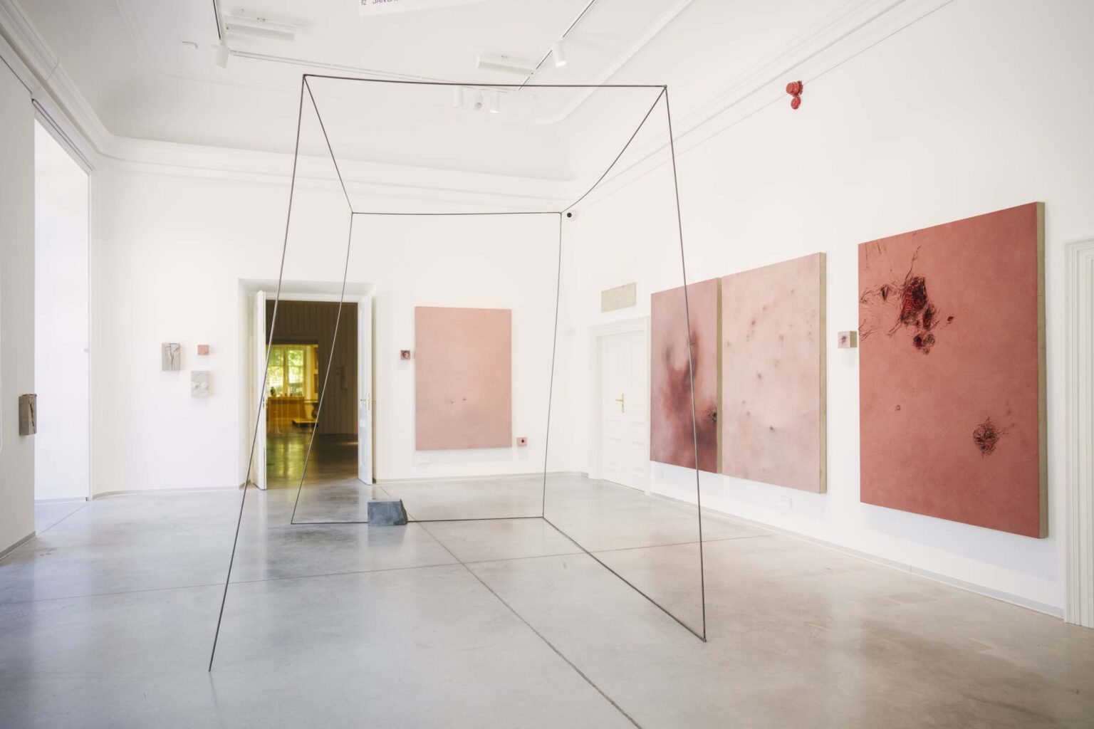 Dużych rozmiarów instalacja z metalowych prętów, na ścianach przestrzenne, dużych rozmiarów obrazy pionowe o odcieniach różu