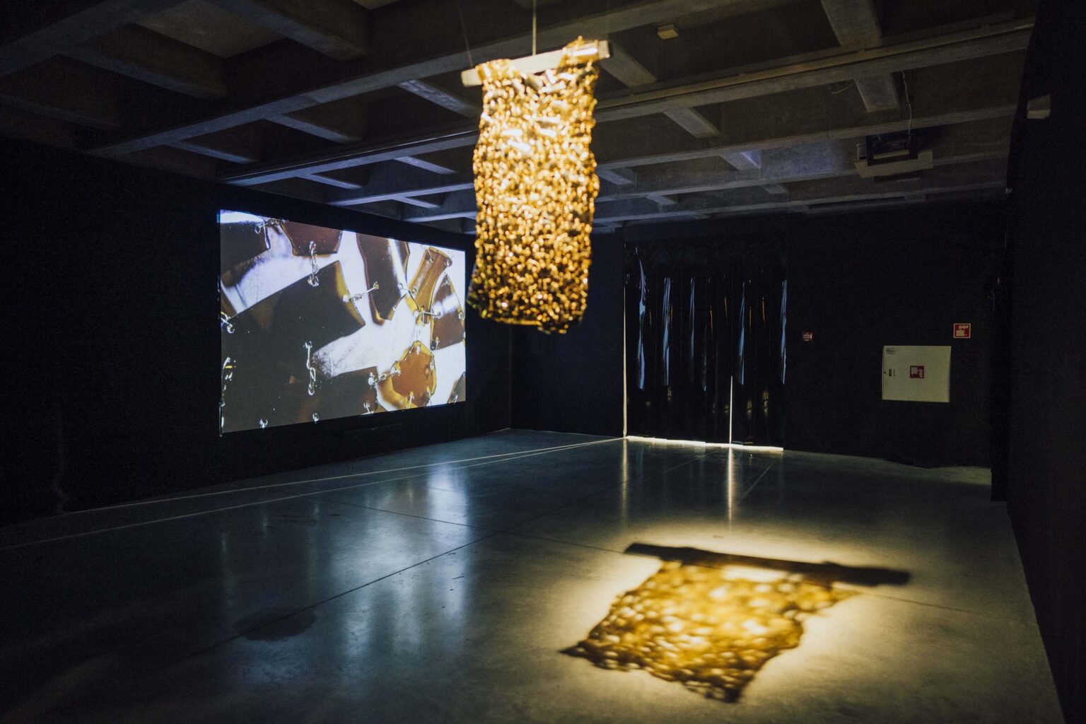 obiekt wiszący zbudowany z żółtych elementów szklanych, rzut obiektu na podłodze, z tyłu projekcja video