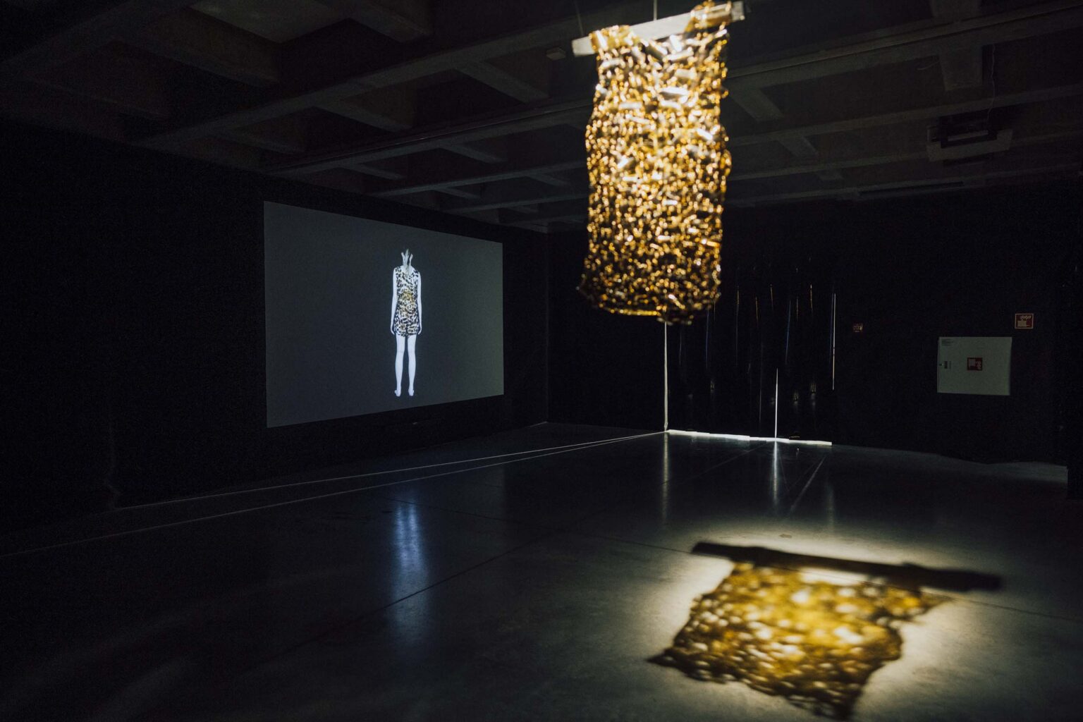 obiekt wiszący zbudowany z żółtych elementów szklanych, rzut obiektu na podłodze, z tyłu projekcja video