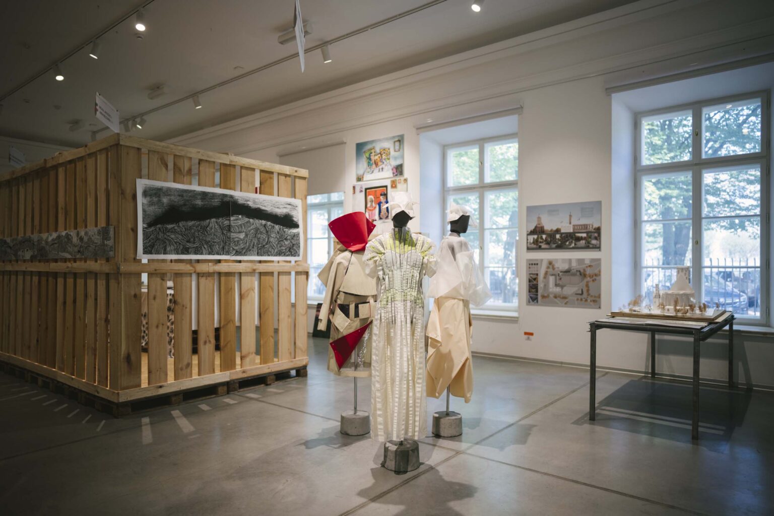 Trzy sylwetki (kostiumy) na manekinach, wystawa w tle