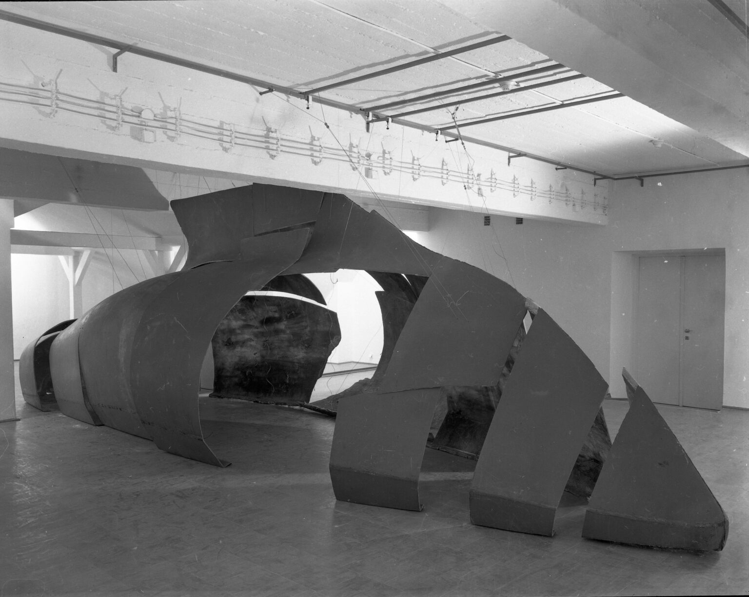 czarno-biała fotografia przedstawia duży obiekt wypełniający po sufit pomieszczenie galerii