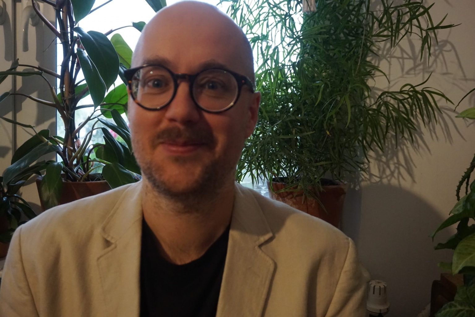 Portret uśmiechniętego mężczyzny w okularach. Rośliny doniczkowe przed