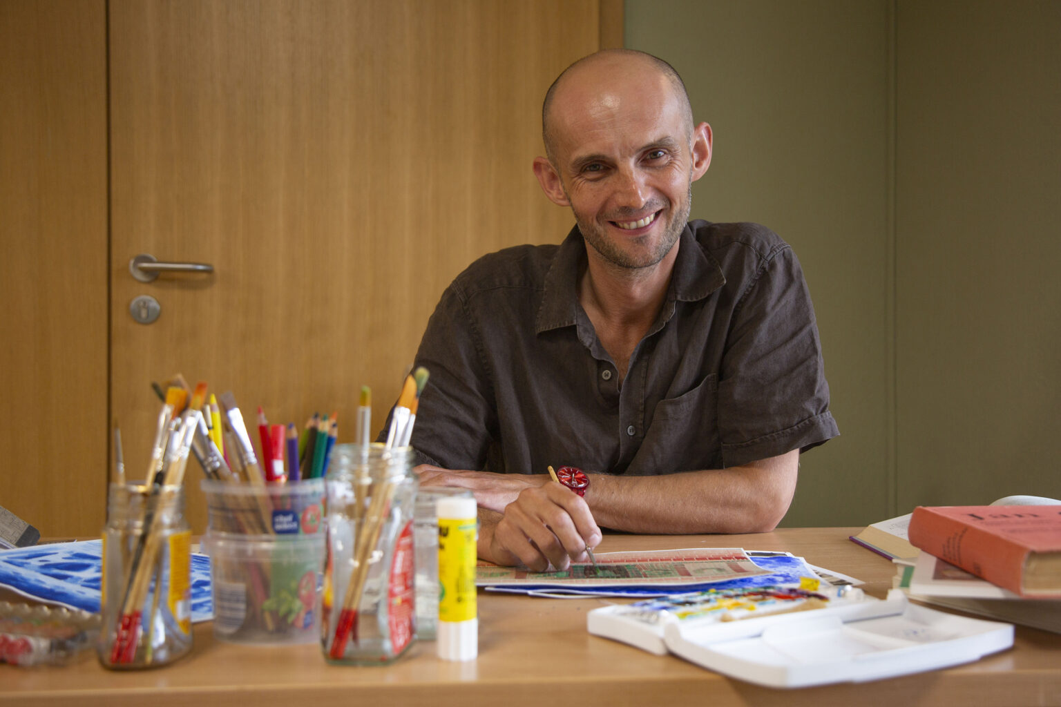 Uśmiechnięty mężczyzna siedzi przy biurku z przyborami do rysowania