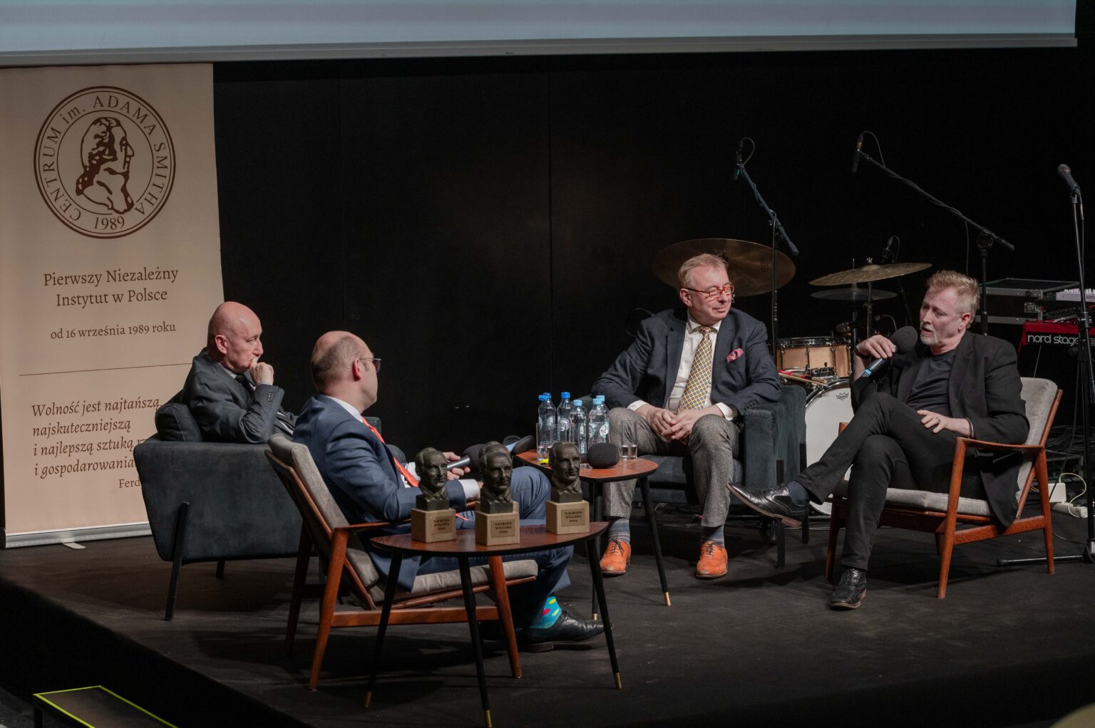 czterech mężczyzn siedzi na krzesłąch i debatuje