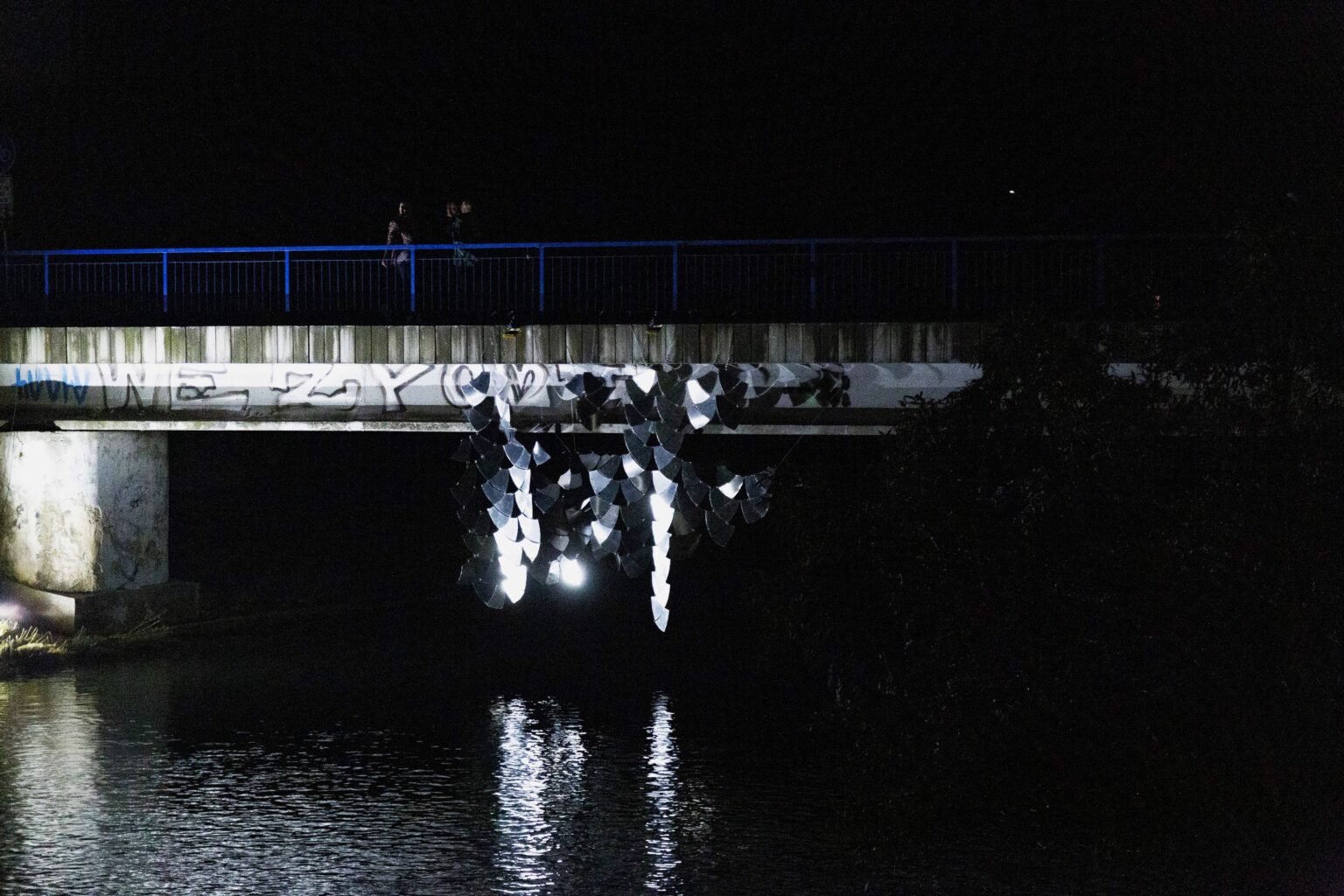 instalacja odbijająca światło powieszona na moście nocą