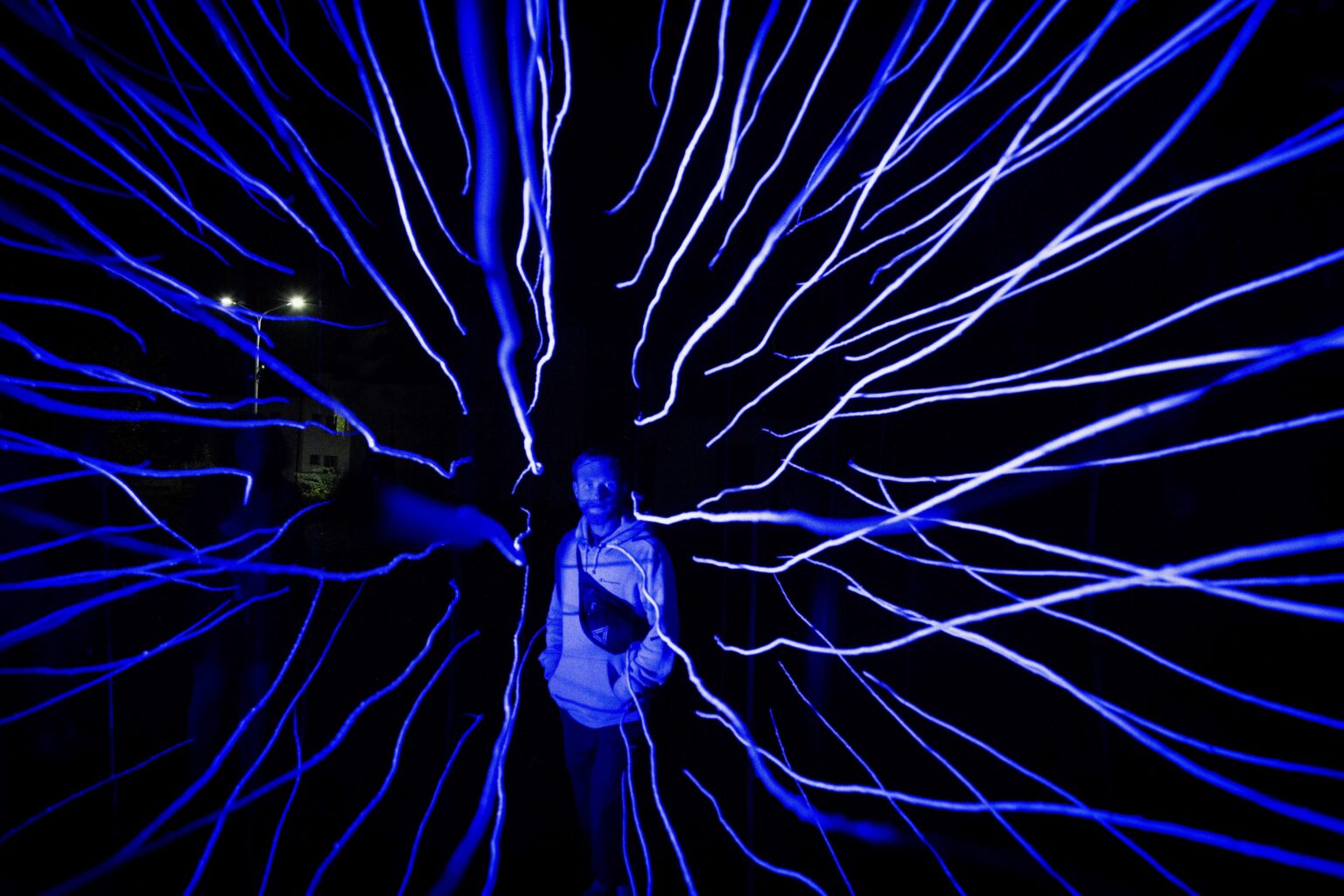 postać mężczyzny w środku niebieskiej, promienistej instalacji świetlnej