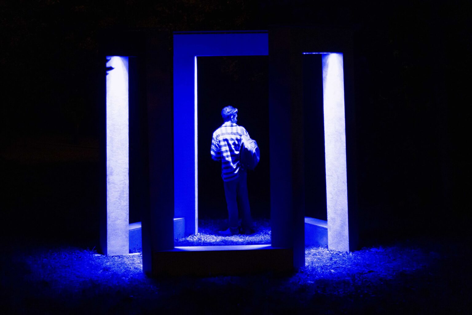 noc. odwrócona tyłem postać wewnątrz geometrycznej instalacji podświetlonej na niebiesko