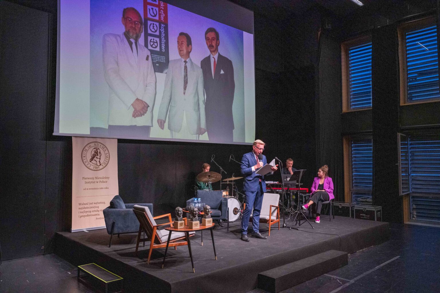 osoby na scenie, nad nimi w tle materiał video na ekranie