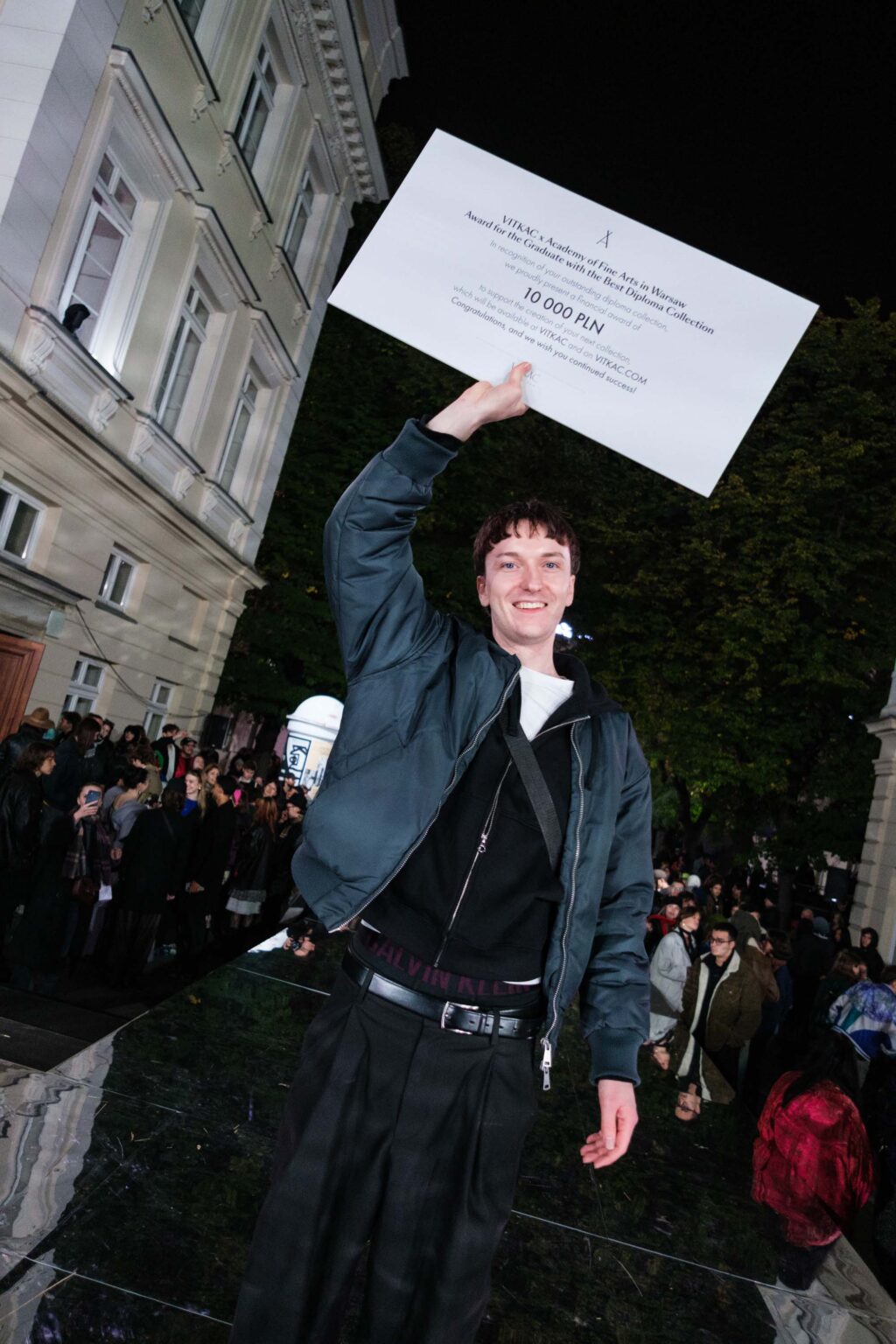 uśmiechnięty młody mężczyzna trzyma nad głową informację o wygranej