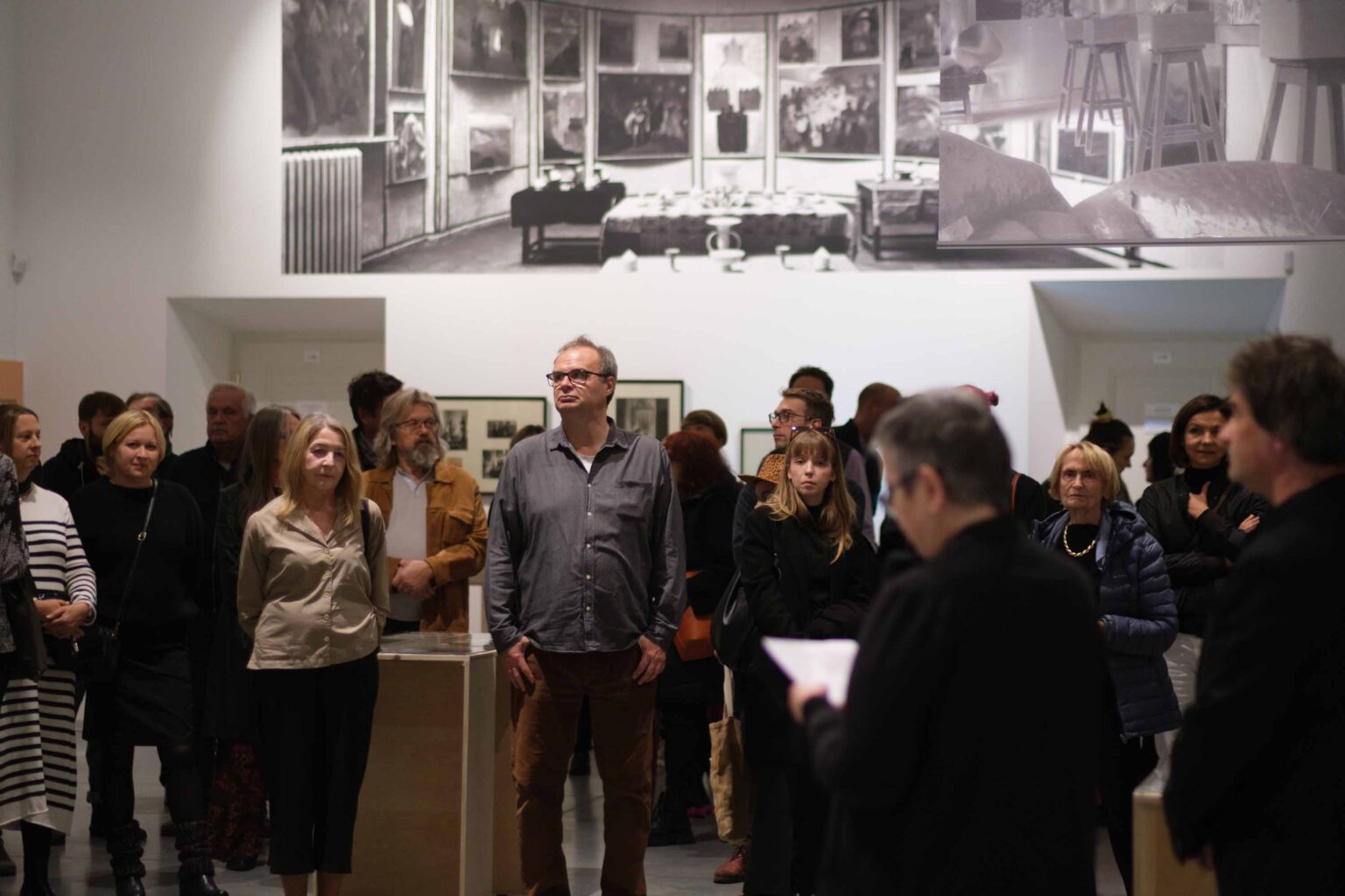 duża grupa zwiedzająćych, wystawa w tle